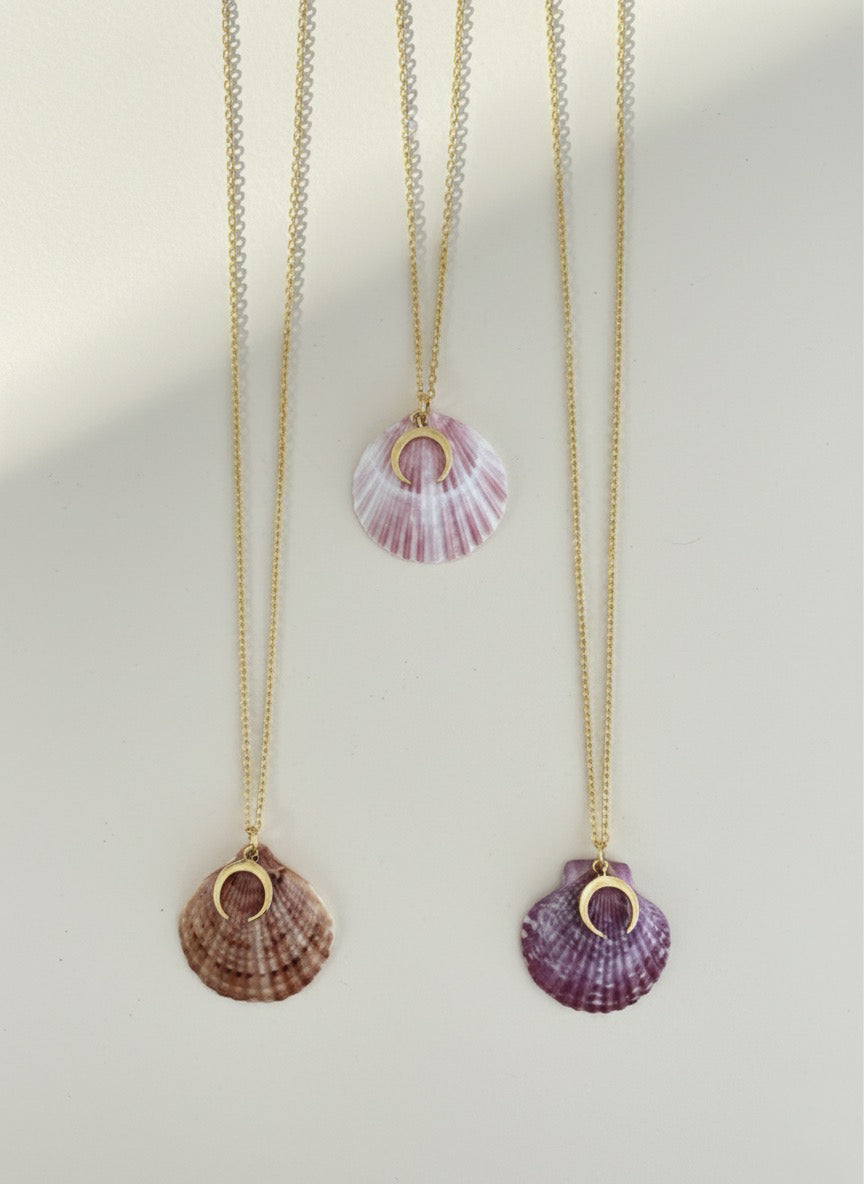 Three shell pendant necklaces on gold chains against a light background
