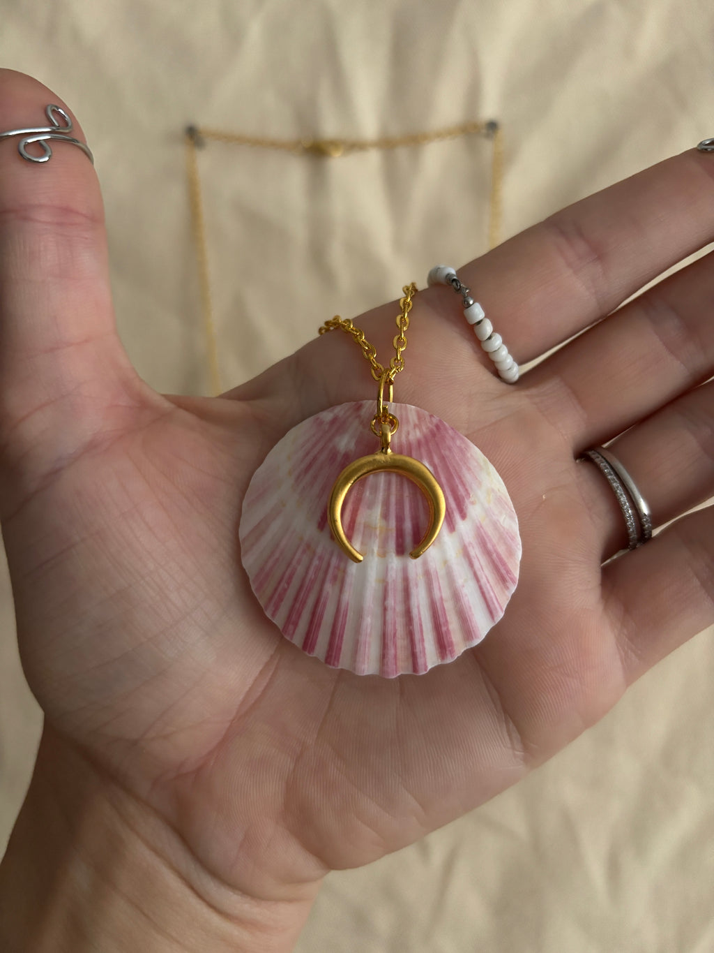 Hand holding a pink shell with a gold crescent moon charm against a neutral background