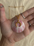 Hand holding a pink shell with a gold crescent moon charm against a neutral background