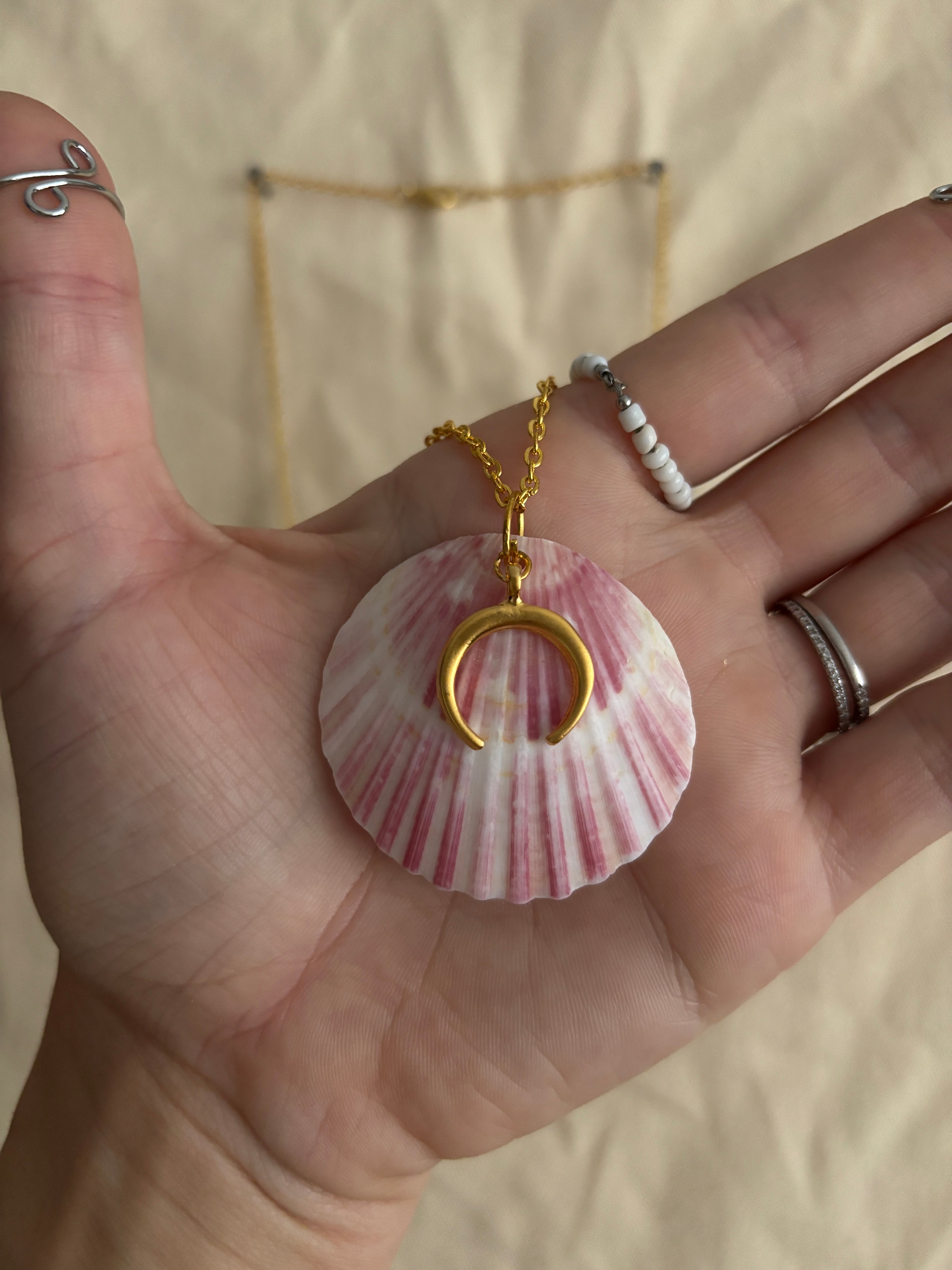 Hand holding a pink shell with a gold crescent moon charm against a neutral background