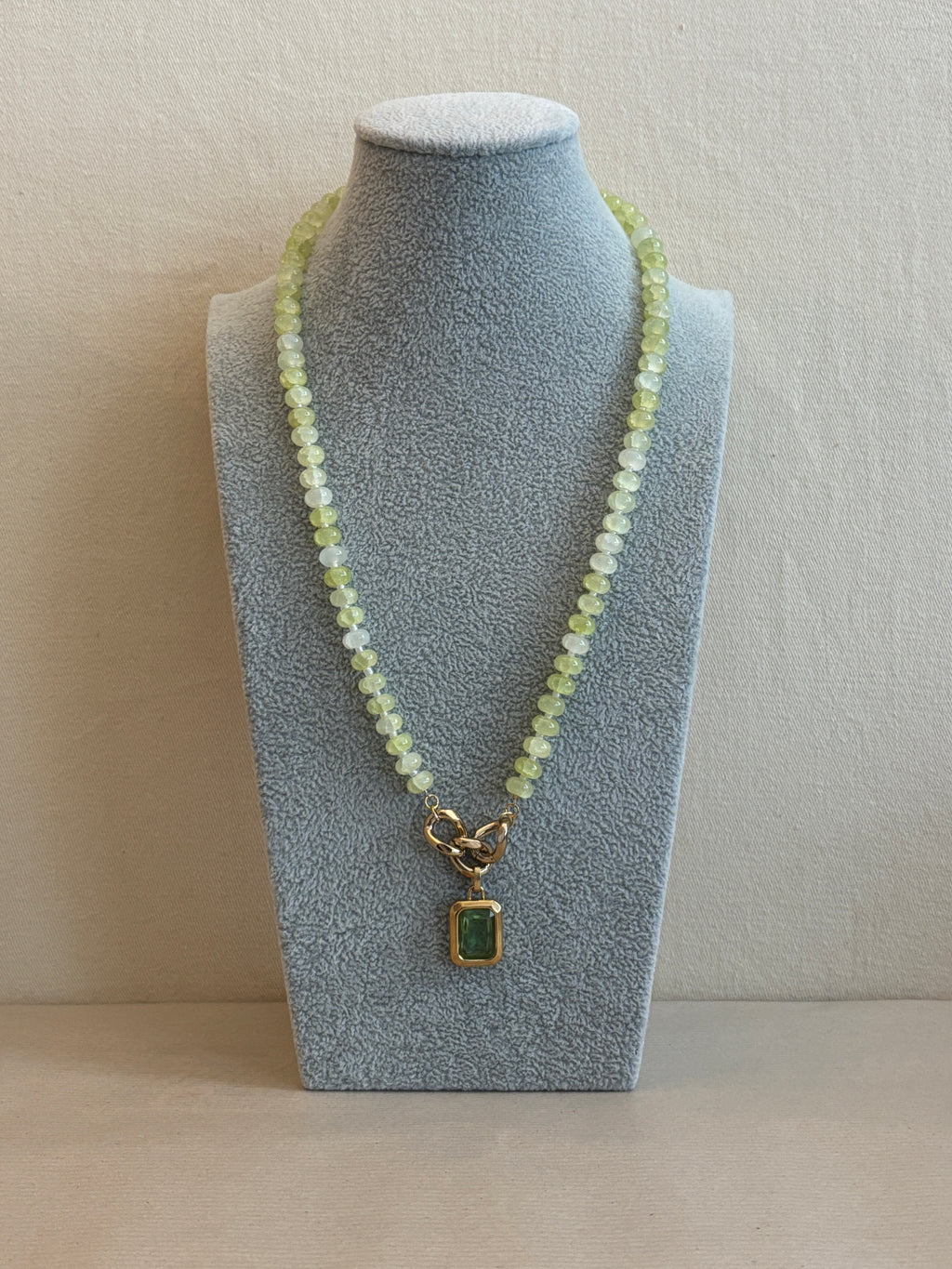 Necklace with a green gemstone pendant on a gray stand
