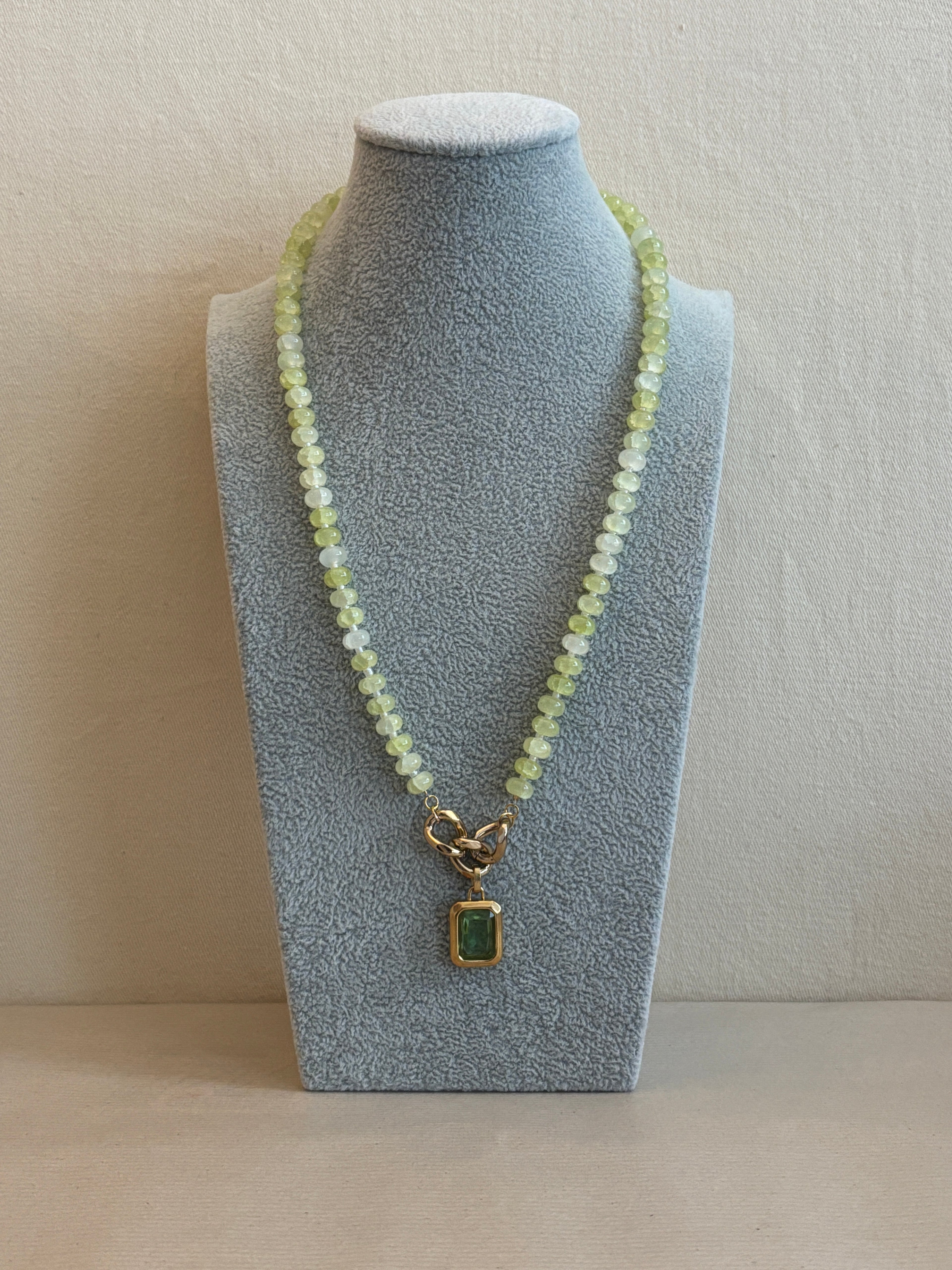 Necklace with a green gemstone pendant on a gray stand