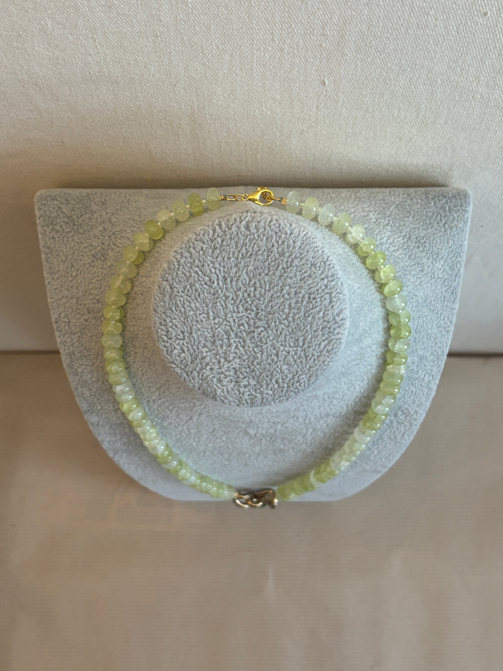 Necklace with green beads on a textured white stand against a beige background