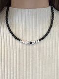 Necklace with beads spelling 'F*CK OFF' on a white ribbed sweater.