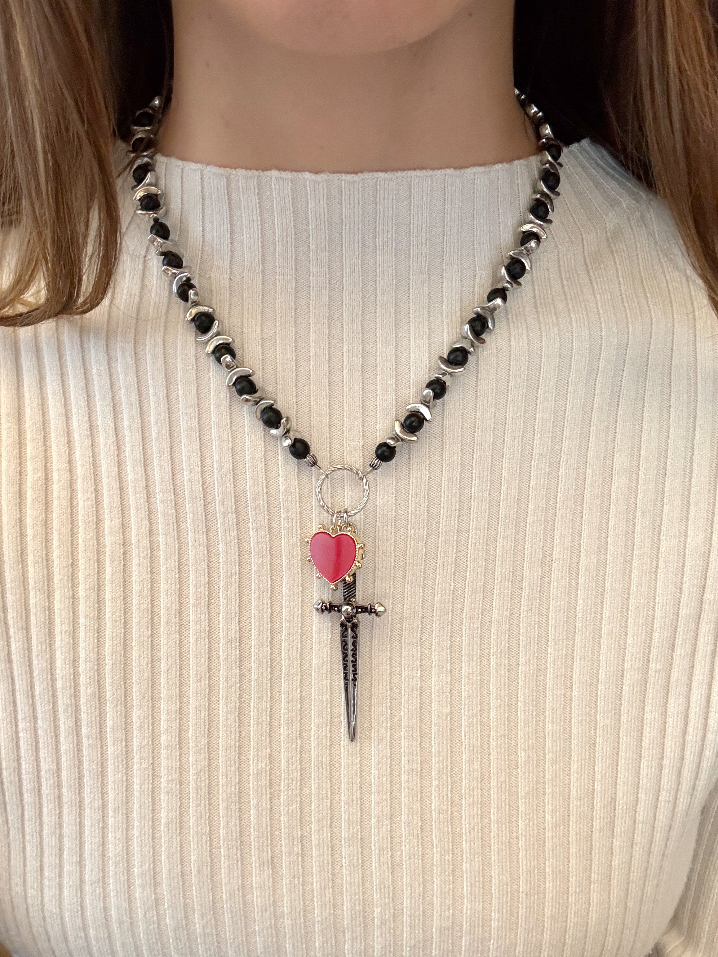 Necklace with black beads and a dagger pendant on a white turtleneck