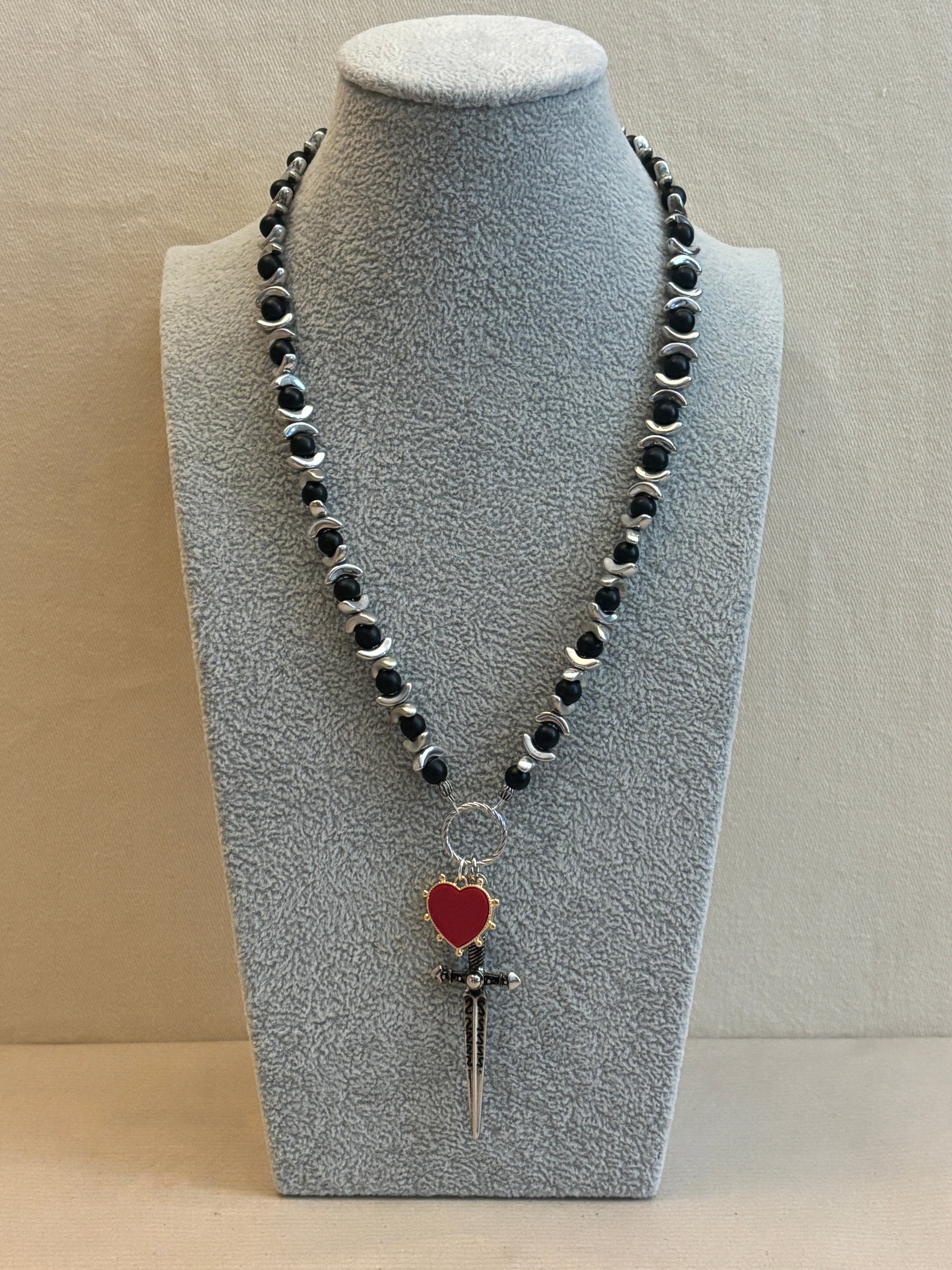 Necklace with a heart pendant on a gray stand against a beige background