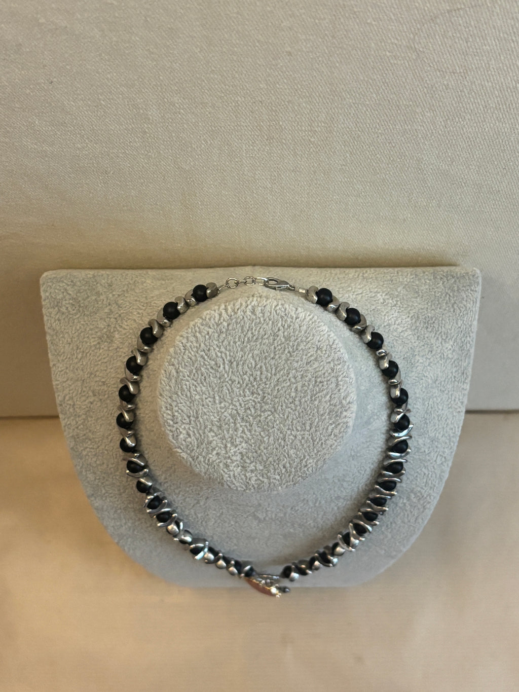Black beaded bracelet on a textured gray stand against a beige background