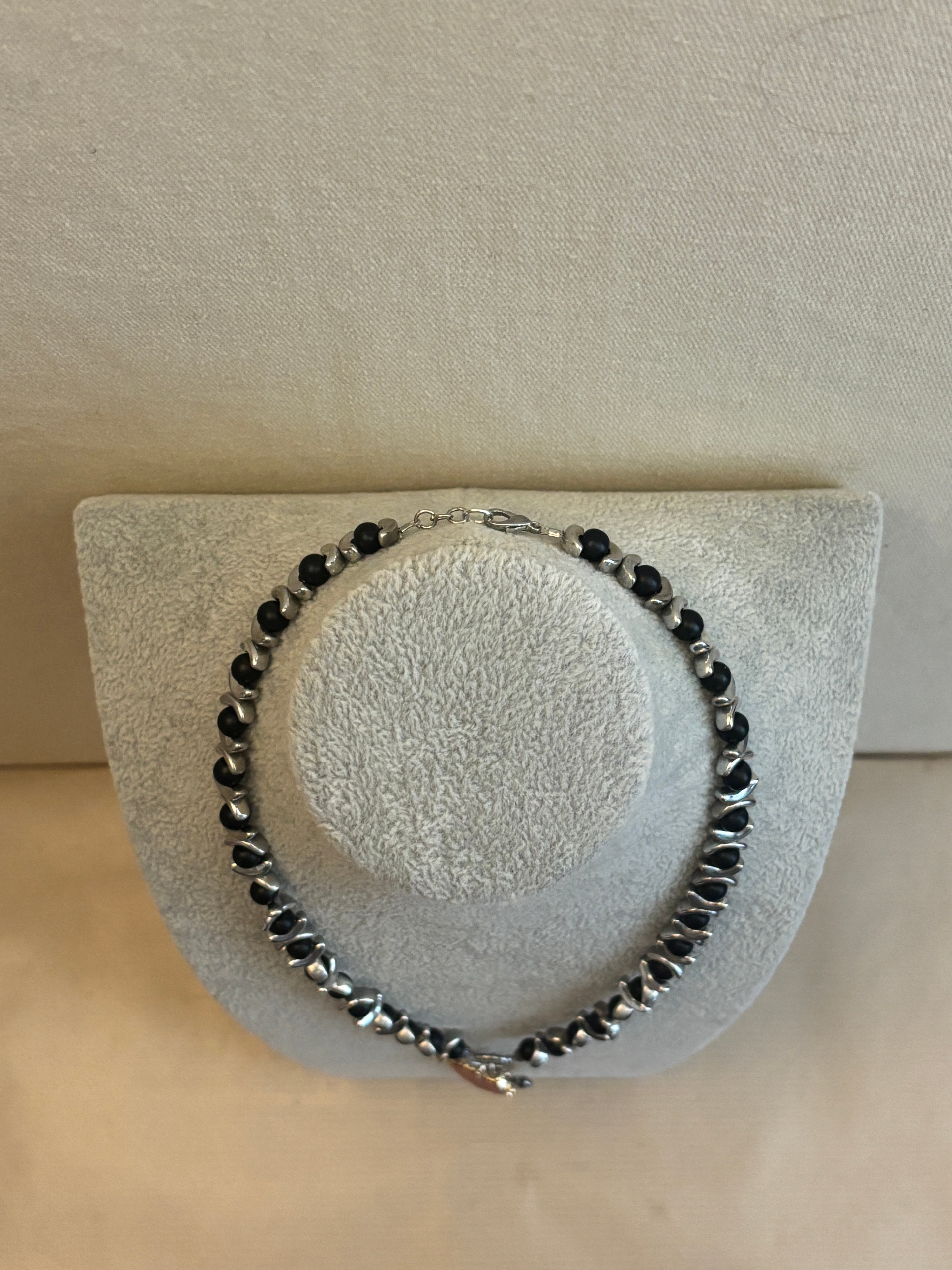 Black beaded bracelet on a textured gray stand against a beige background