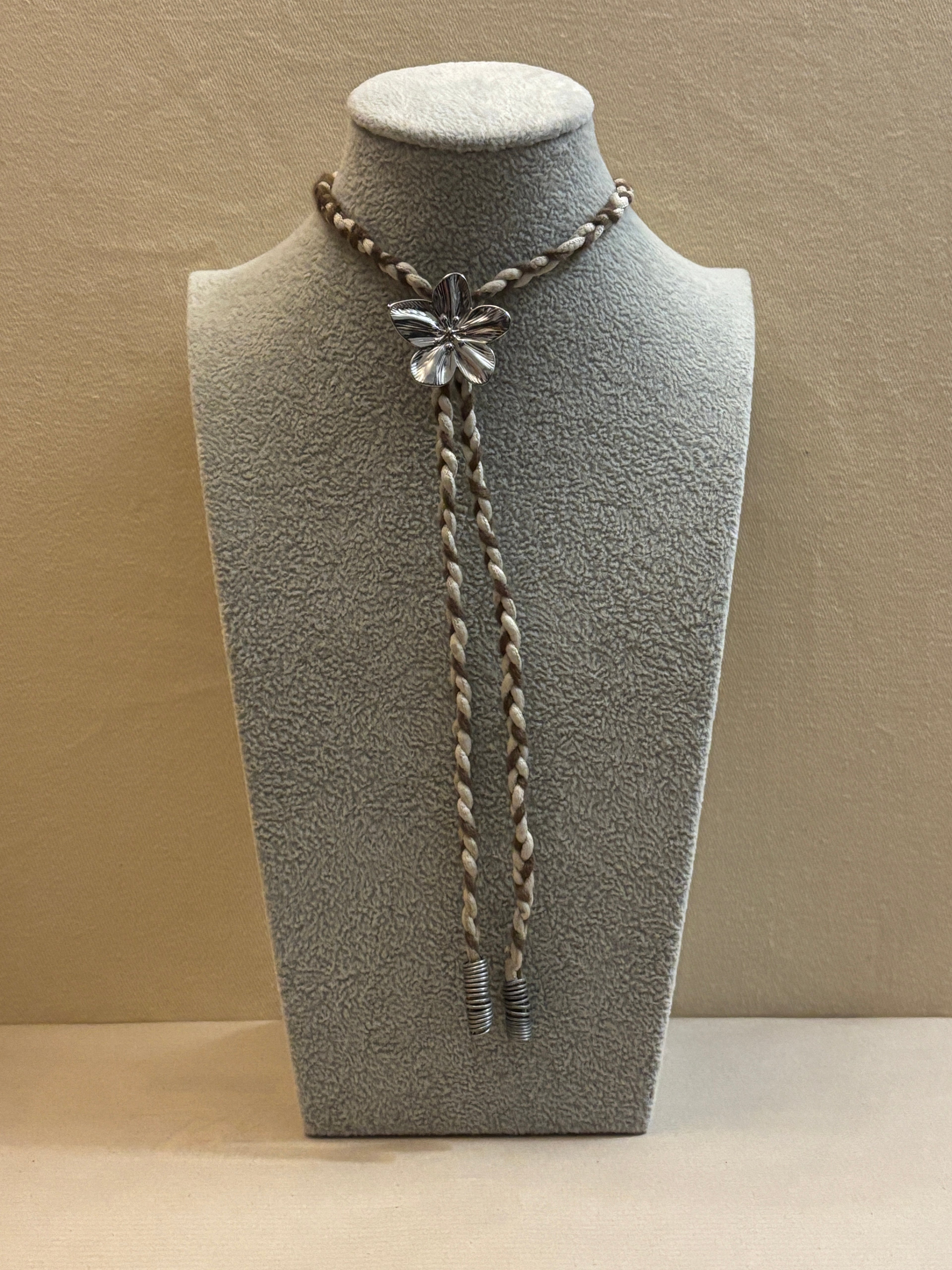 Silver bolo tie on a gray bust against a beige background