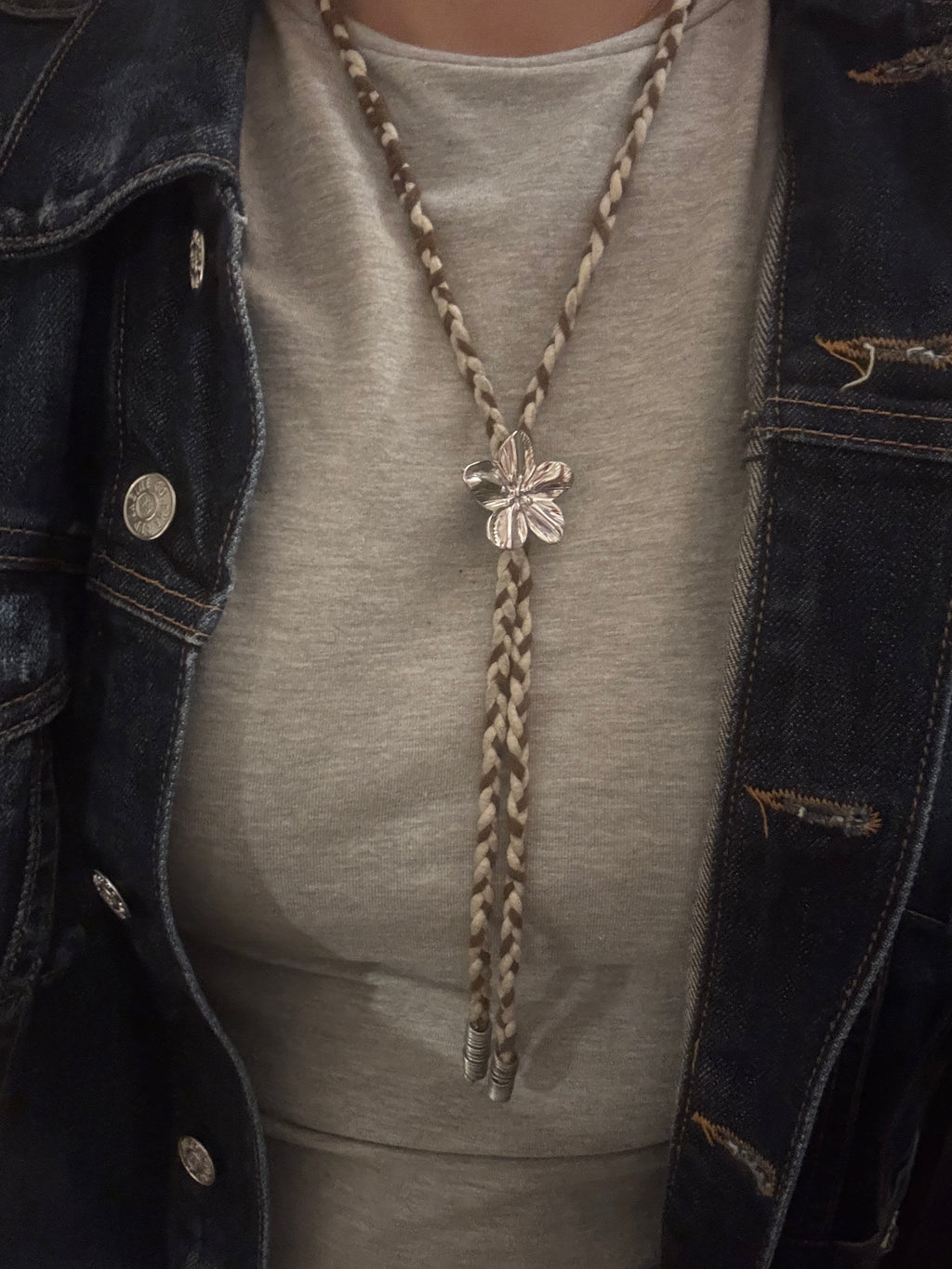 Close-up of a person wearing a denim jacket with a decorative braid and silver brooch.