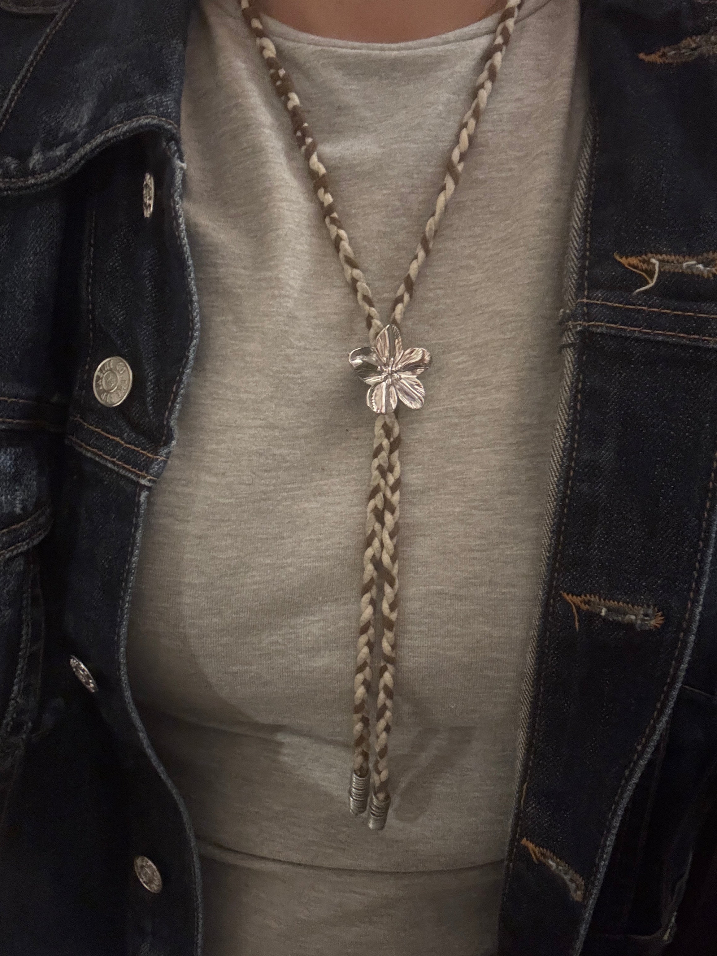 Close-up of a person wearing a denim jacket with a decorative braid and silver brooch.