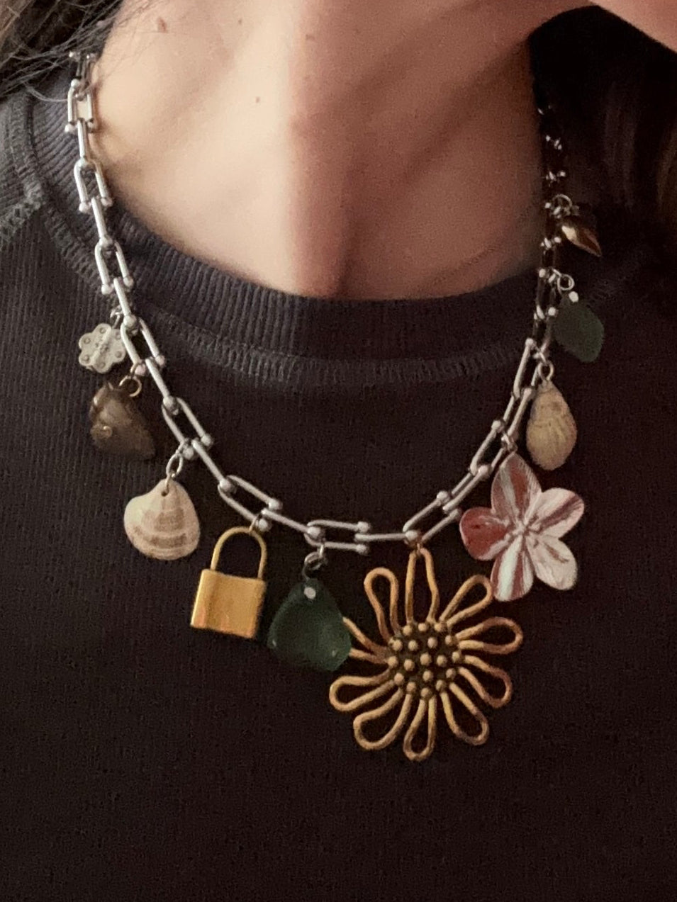 Necklace with various charms including a flower and lock on a dark background