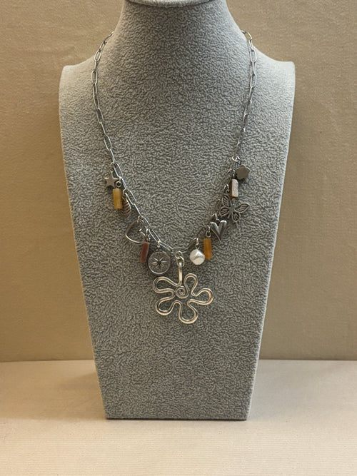 Silver necklace with charms on a gray mannequin bust against a beige background