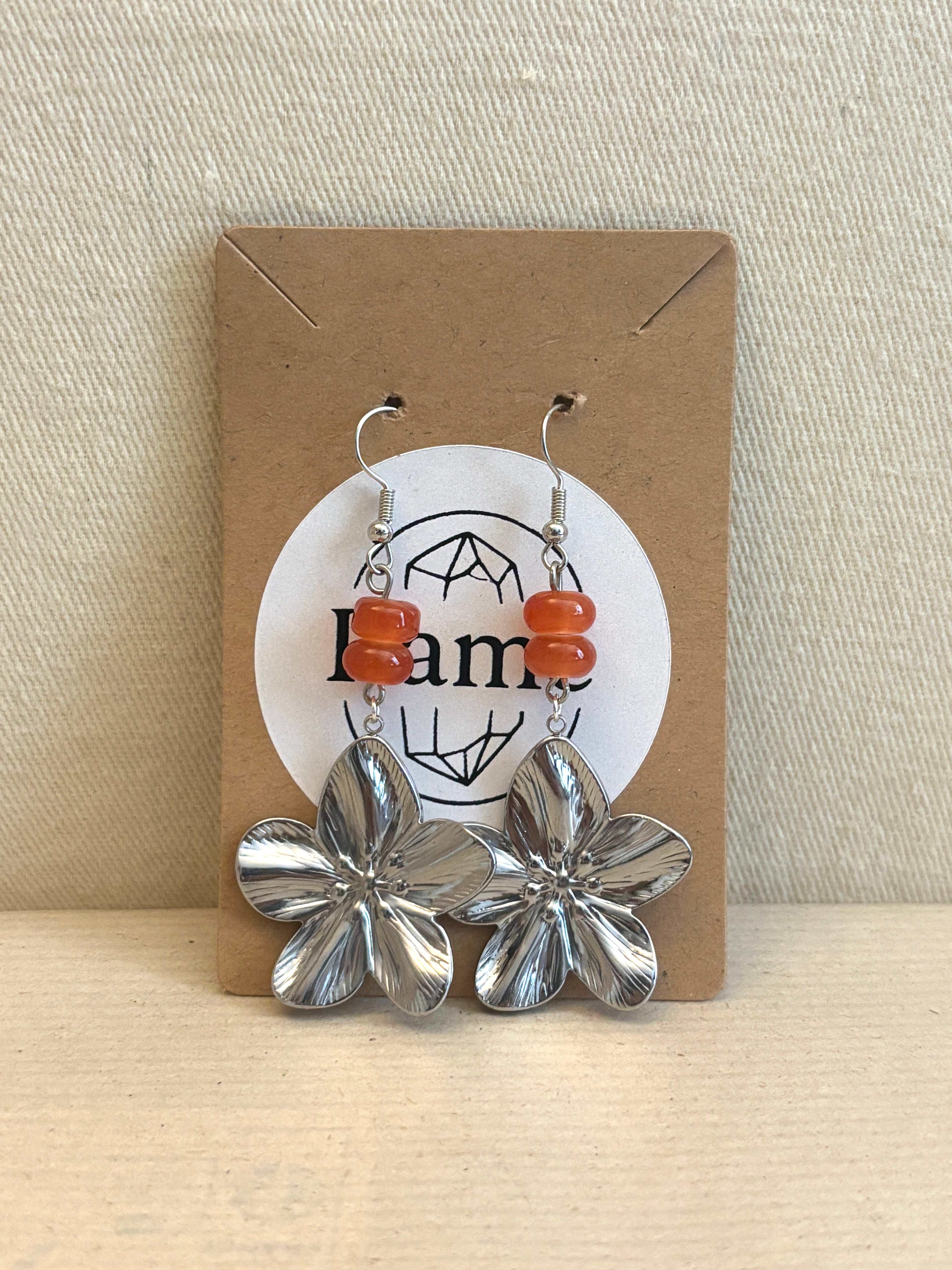 Flower-shaped earrings on a Ramé branded card with a beige background