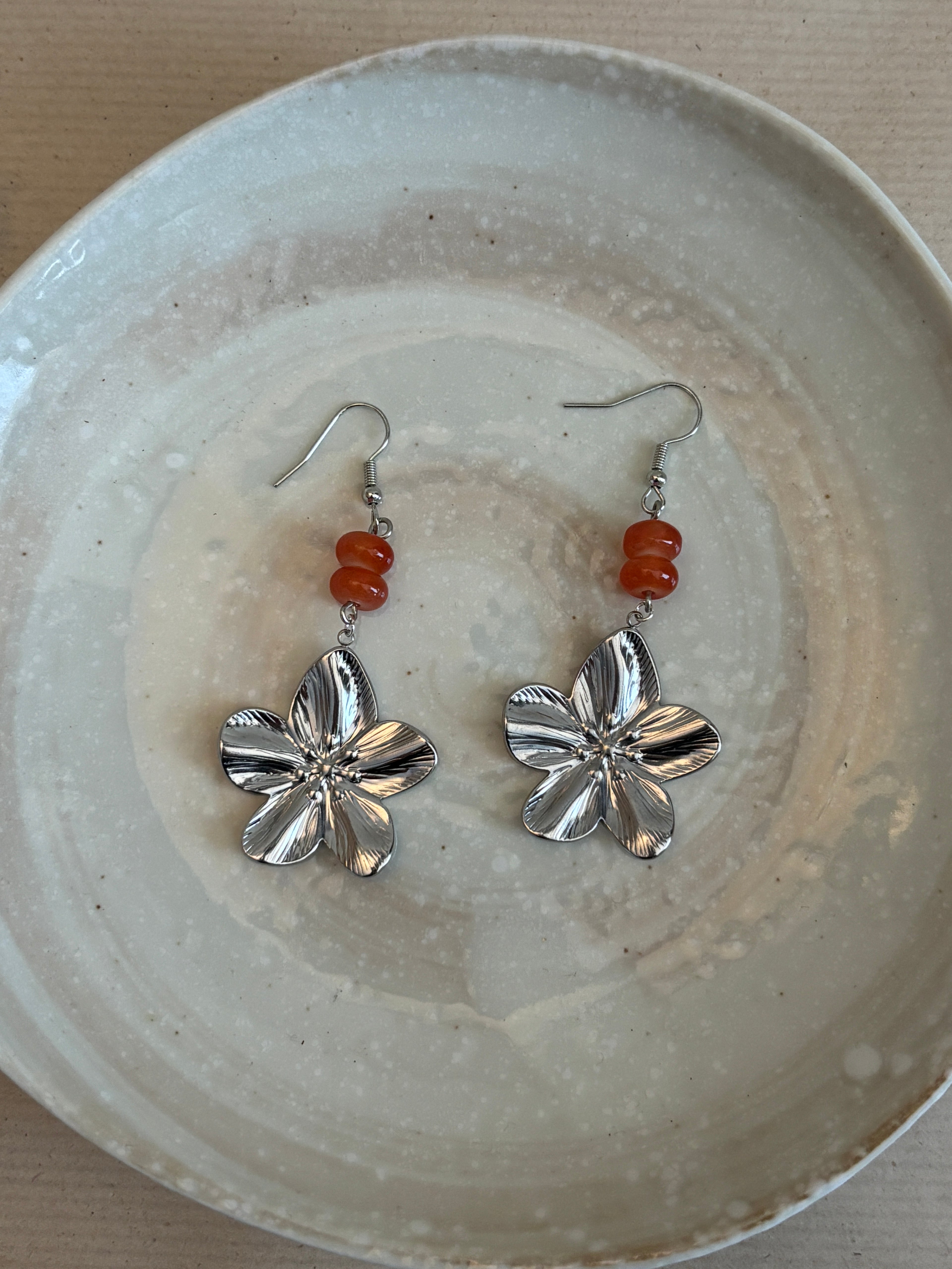 Silver flower-shaped earrings with red beads on a textured white plate.