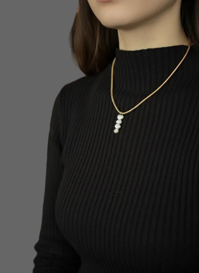 Person wearing a gold necklace with pearls in a blurred indoor setting