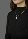 Person wearing a gold necklace with pearls in a blurred indoor setting
