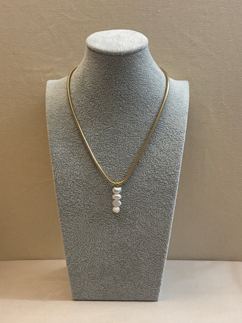 Gray jewelry display stand with gold necklace and white pearls on a beige background