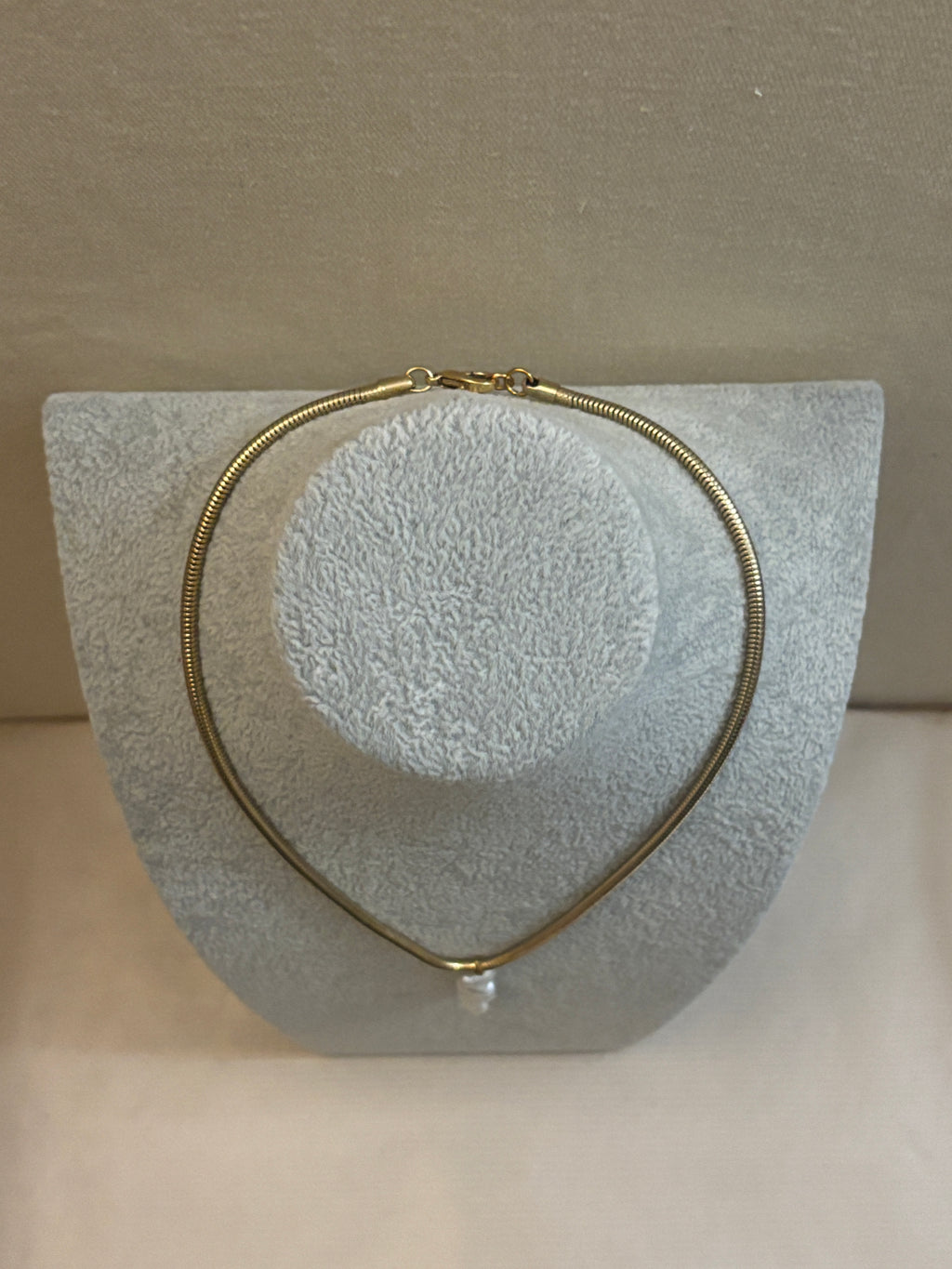 Gold necklace on a textured gray stand against a beige background