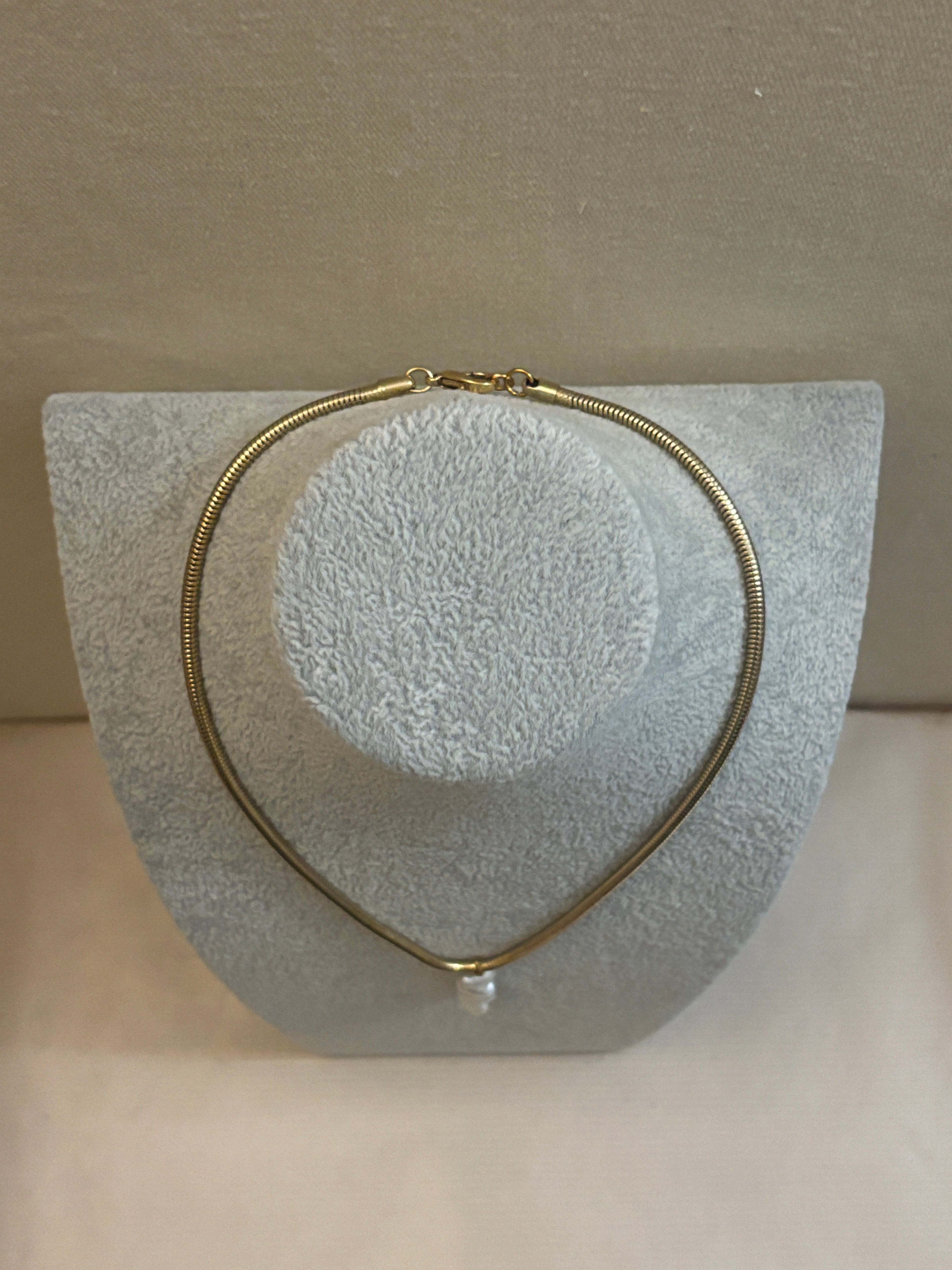 Gold necklace on a textured gray stand against a beige background
