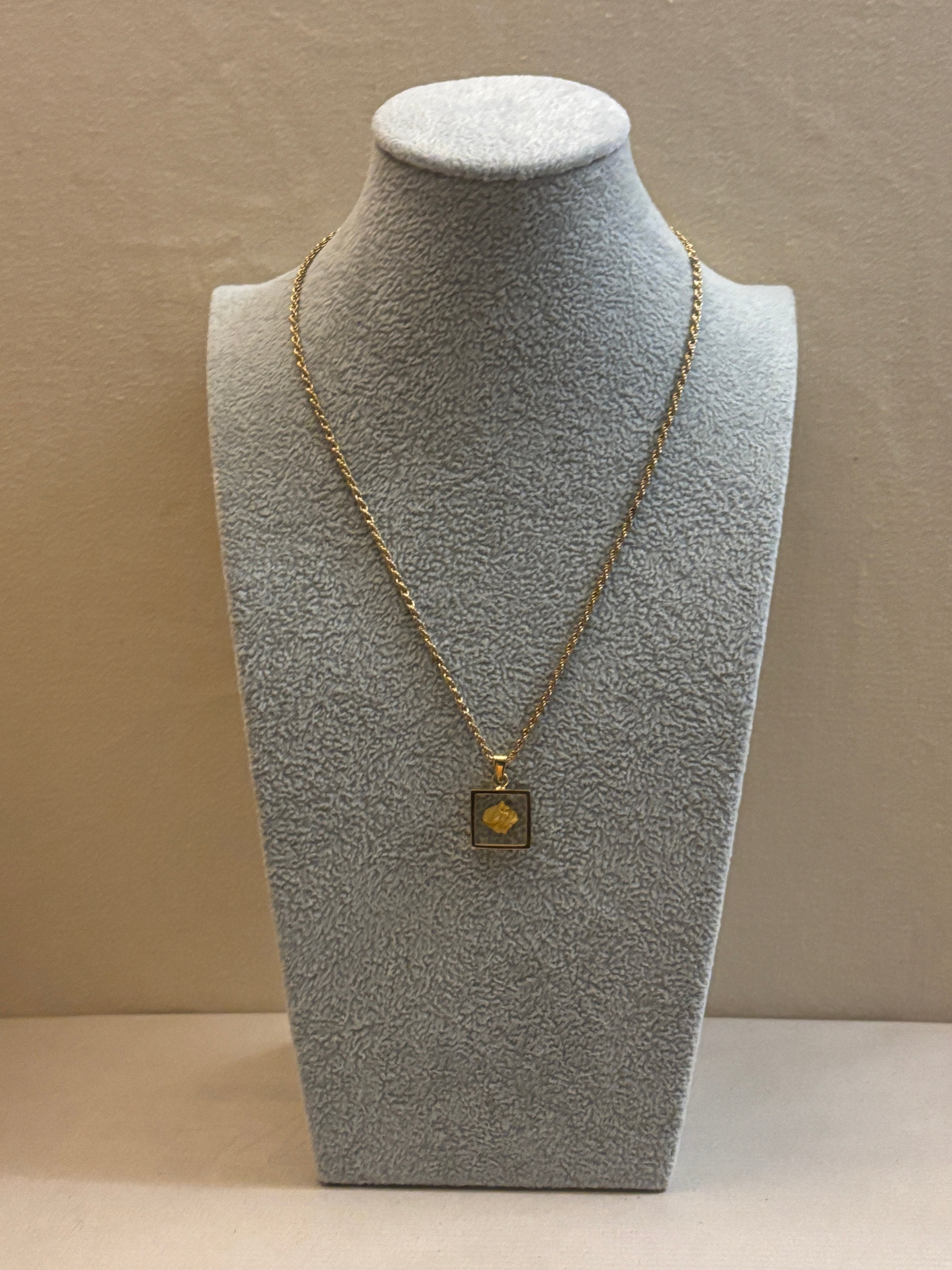 Gold necklace on a gray mannequin bust against a beige background