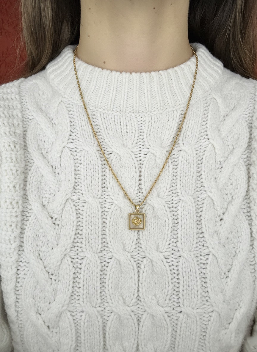 White cable knit sweater with a gold necklace featuring a square pendant.