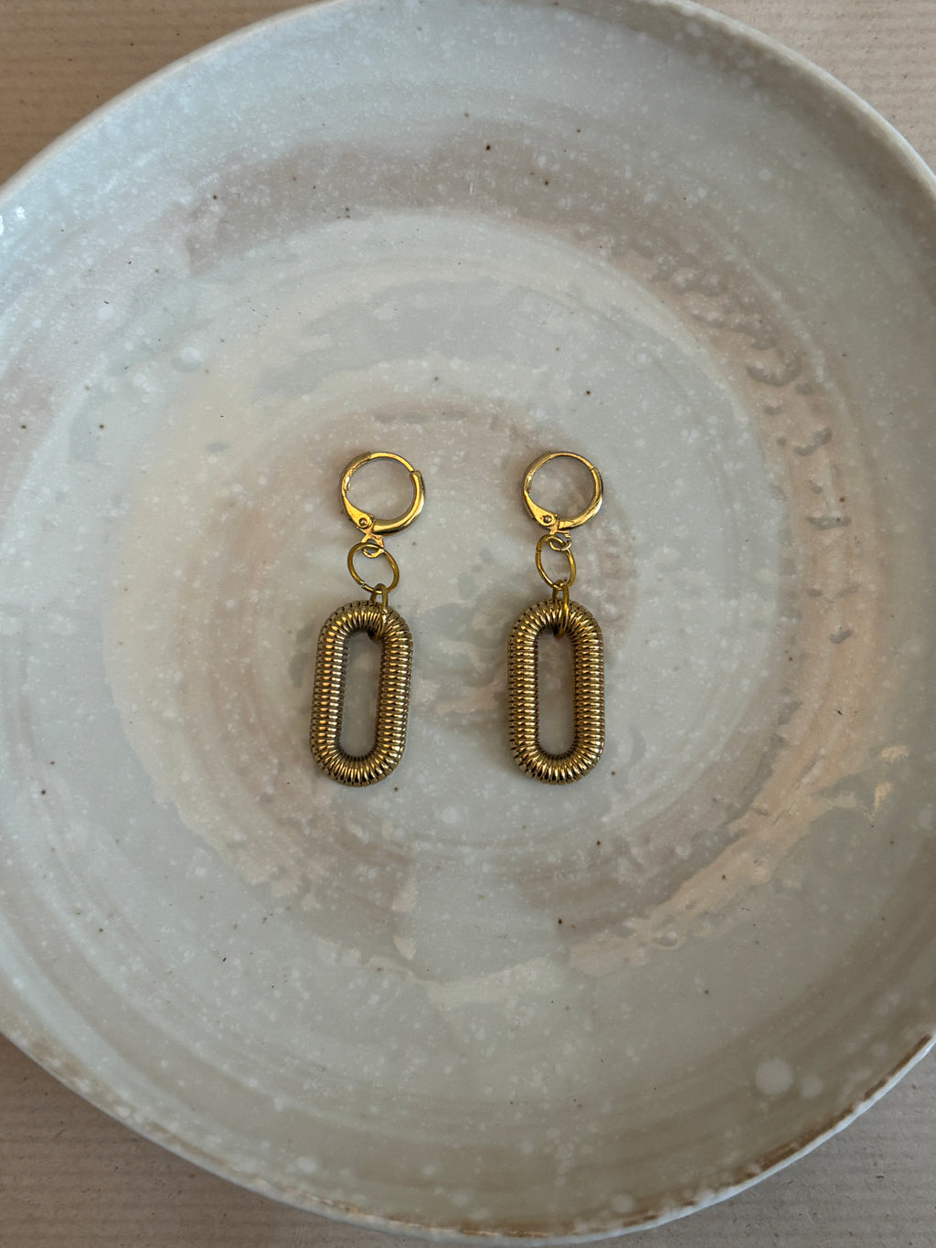 Pair of gold earrings on a textured white plate