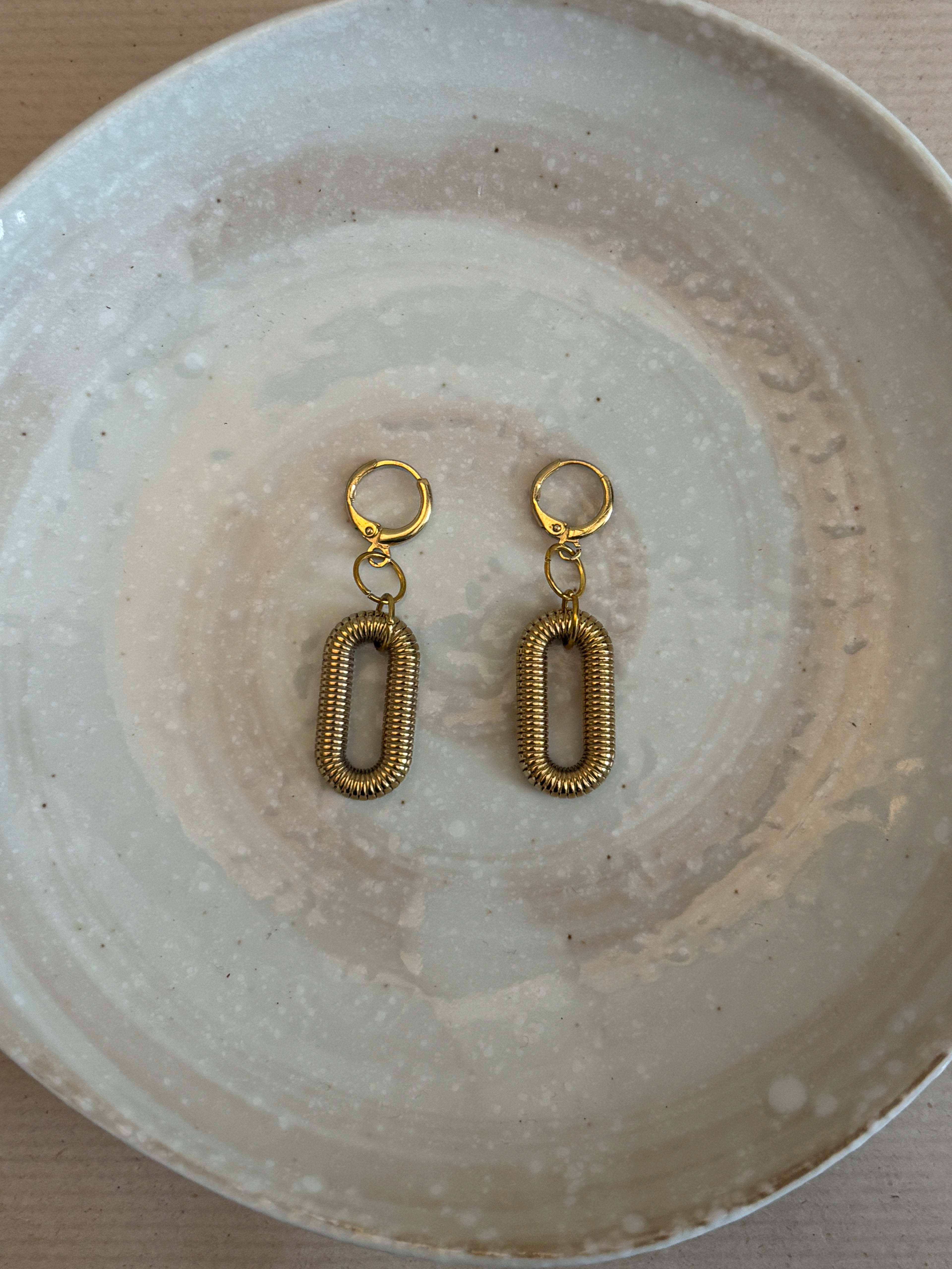Pair of gold earrings on a textured white plate
