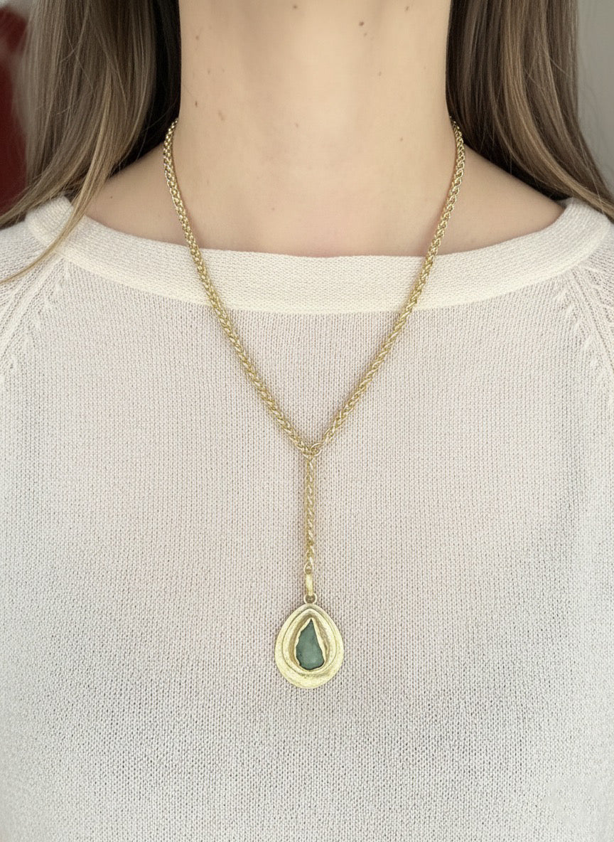 Gold necklace with a green teardrop pendant worn by a person.
