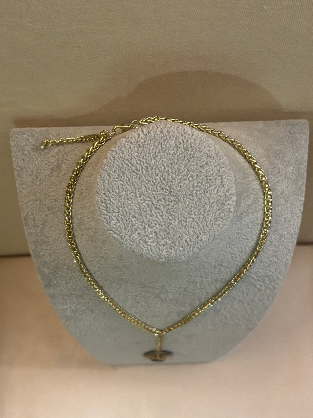 Gold necklace on a textured gray stand against a beige background