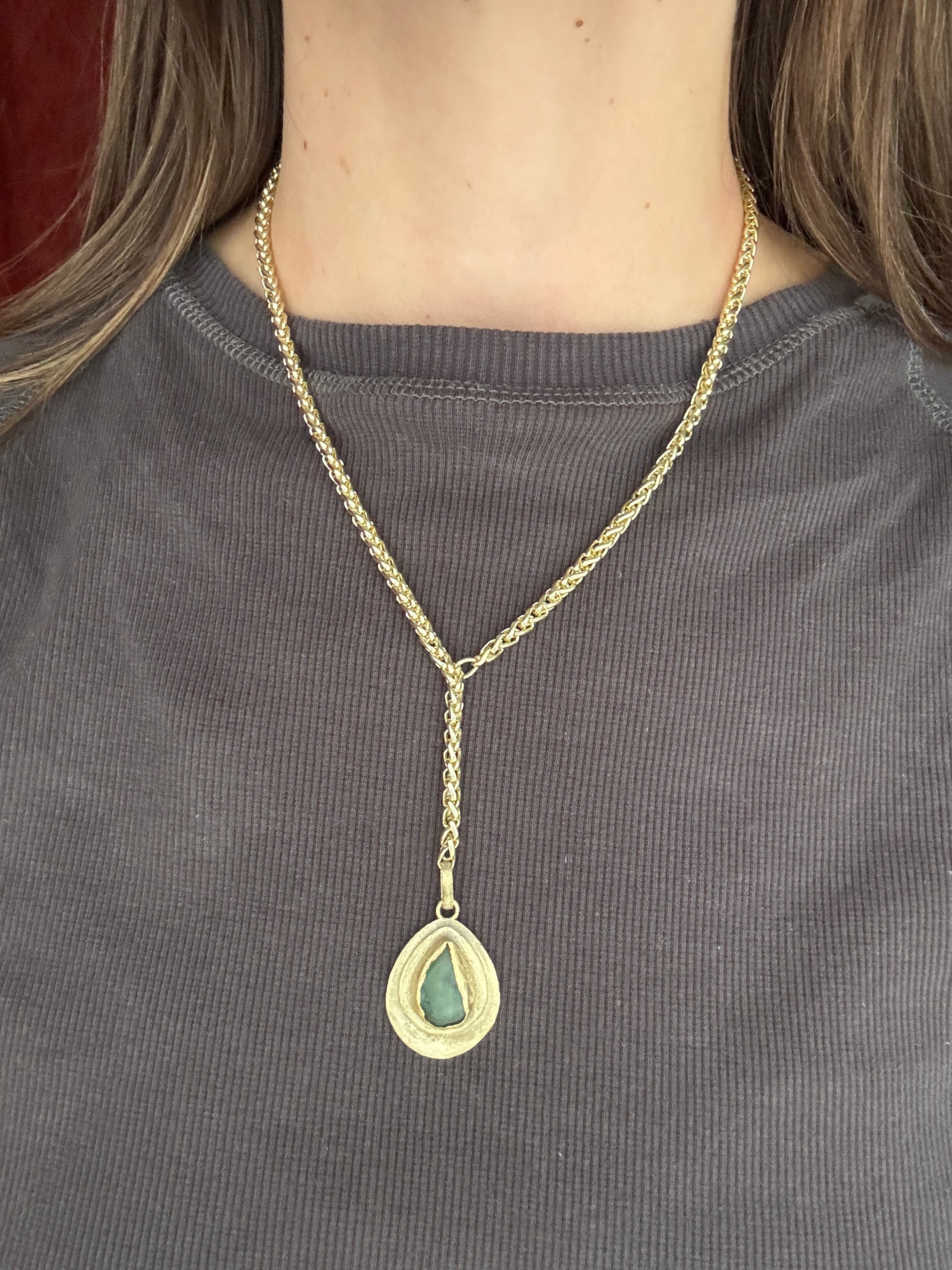 Gold necklace with a green pendant on a gray fabric background