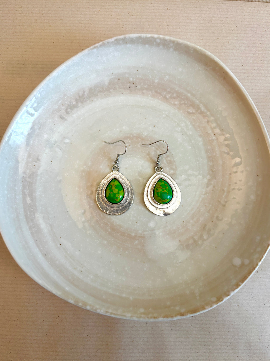 Teardrop-shaped earrings with green gemstones on a textured white plate.