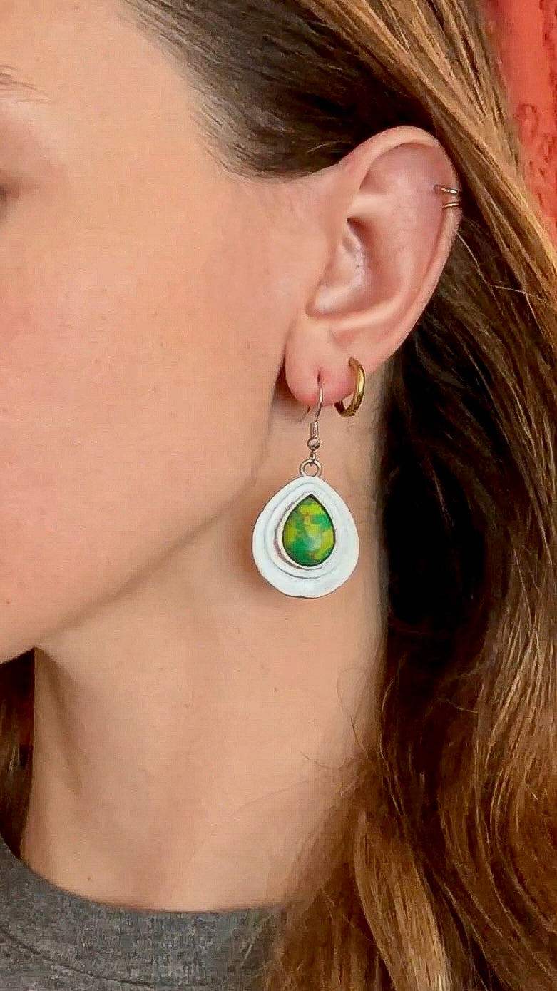 Close-up of a person wearing a teardrop-shaped earring with a green gemstone.