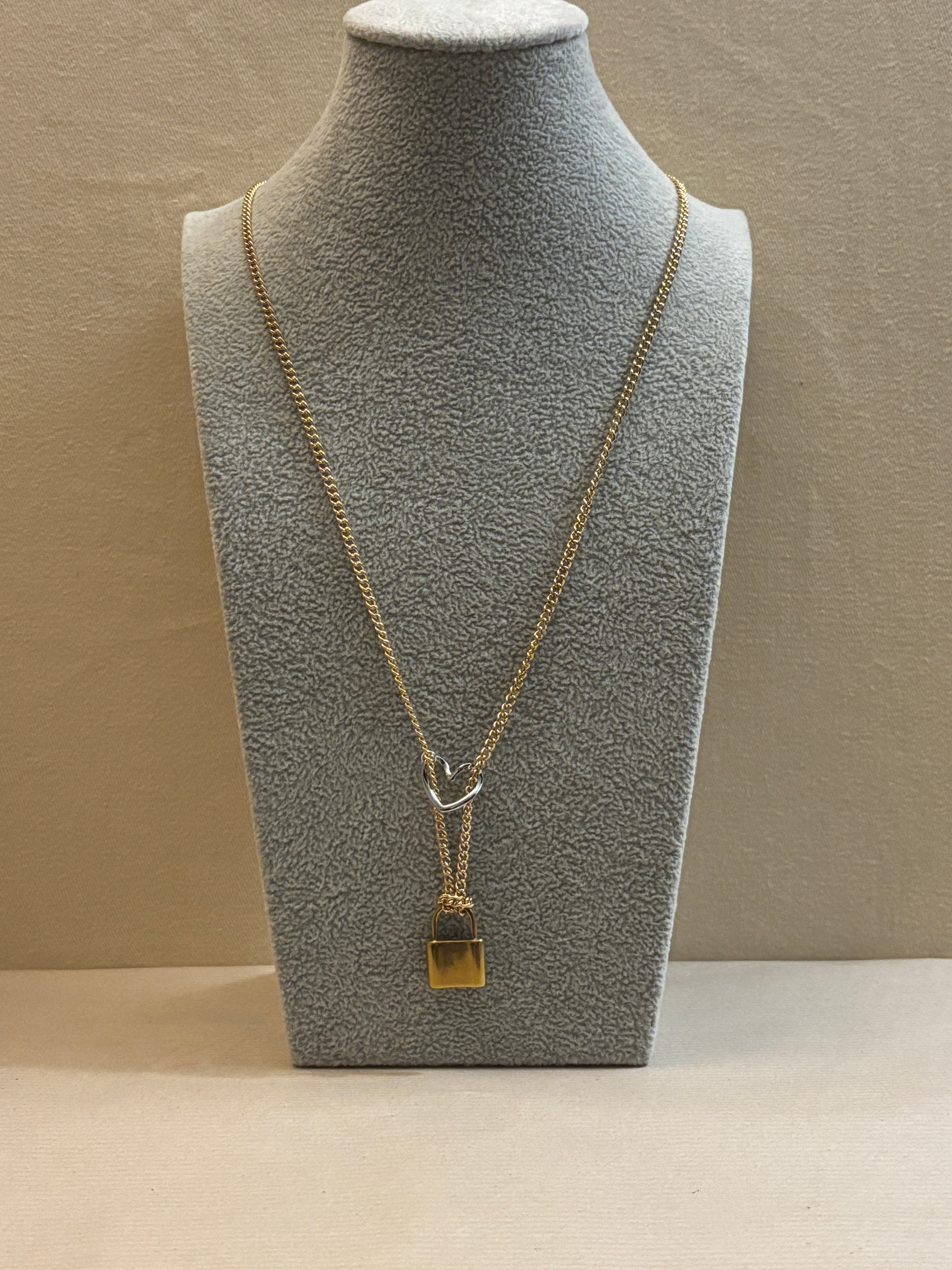 Gold necklace on a gray mannequin bust against a beige wall.