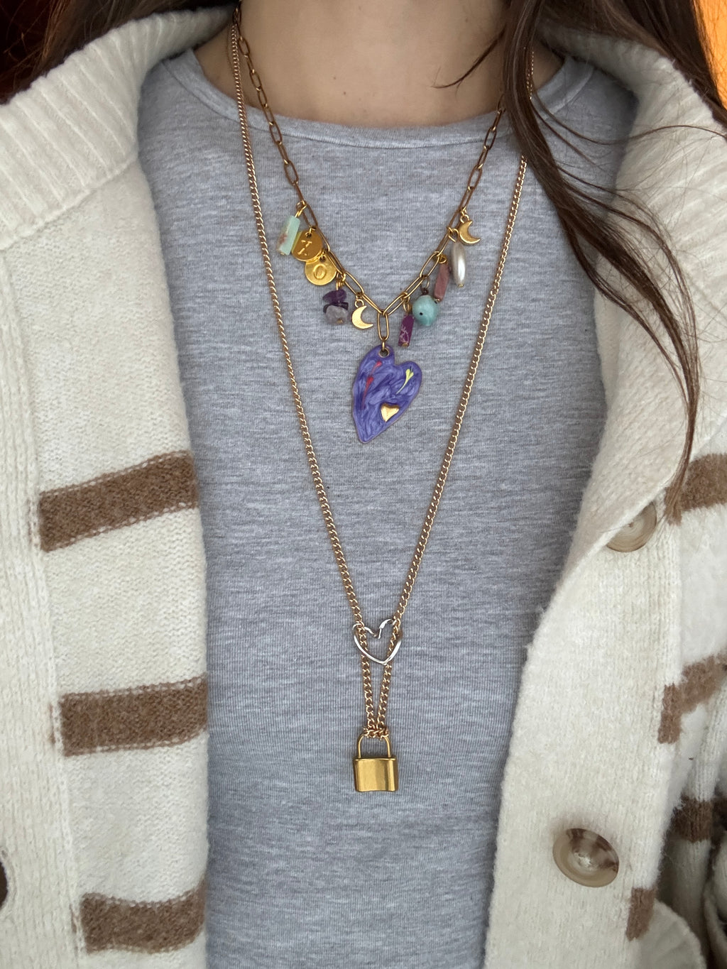 Close-up of a person wearing a gold necklace with charms on a gray sweater.