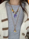 Close-up of a person wearing a gold necklace with charms on a gray sweater.