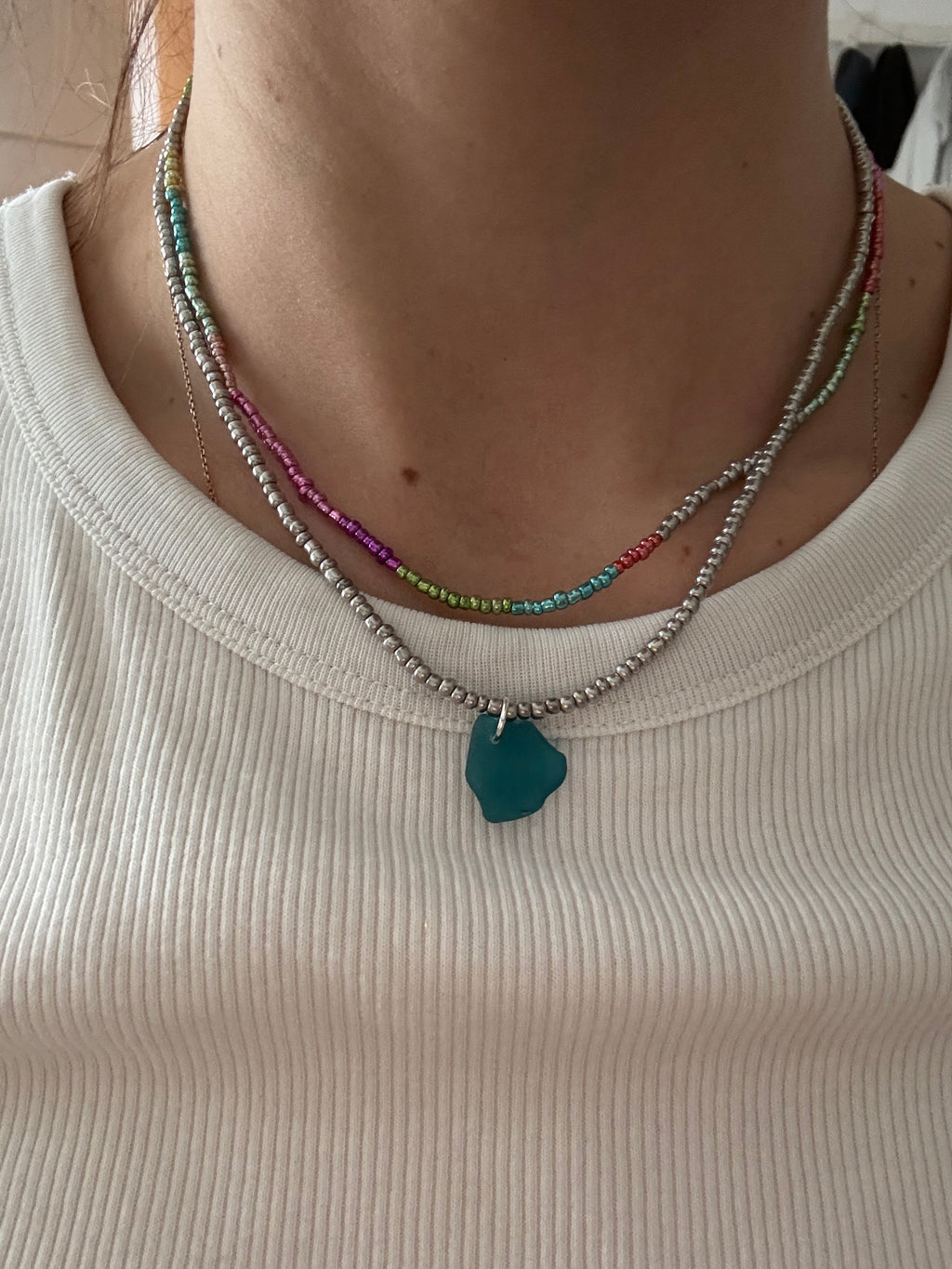 Close-up of a person wearing a necklace with a green pendant on a beige background