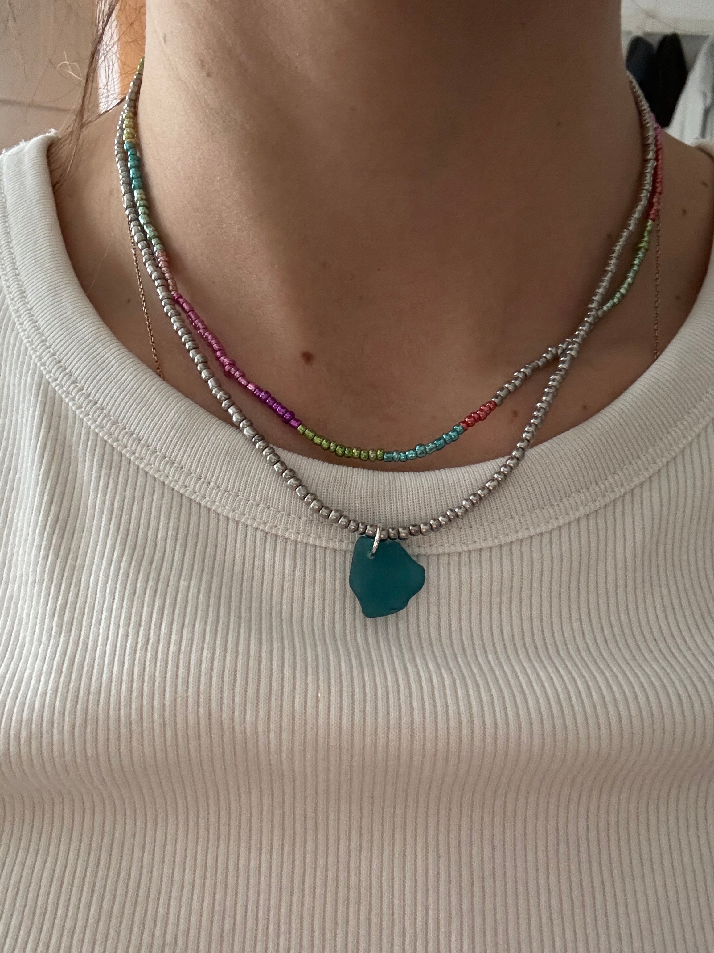 Close-up of a person wearing a necklace with a green pendant on a beige background
