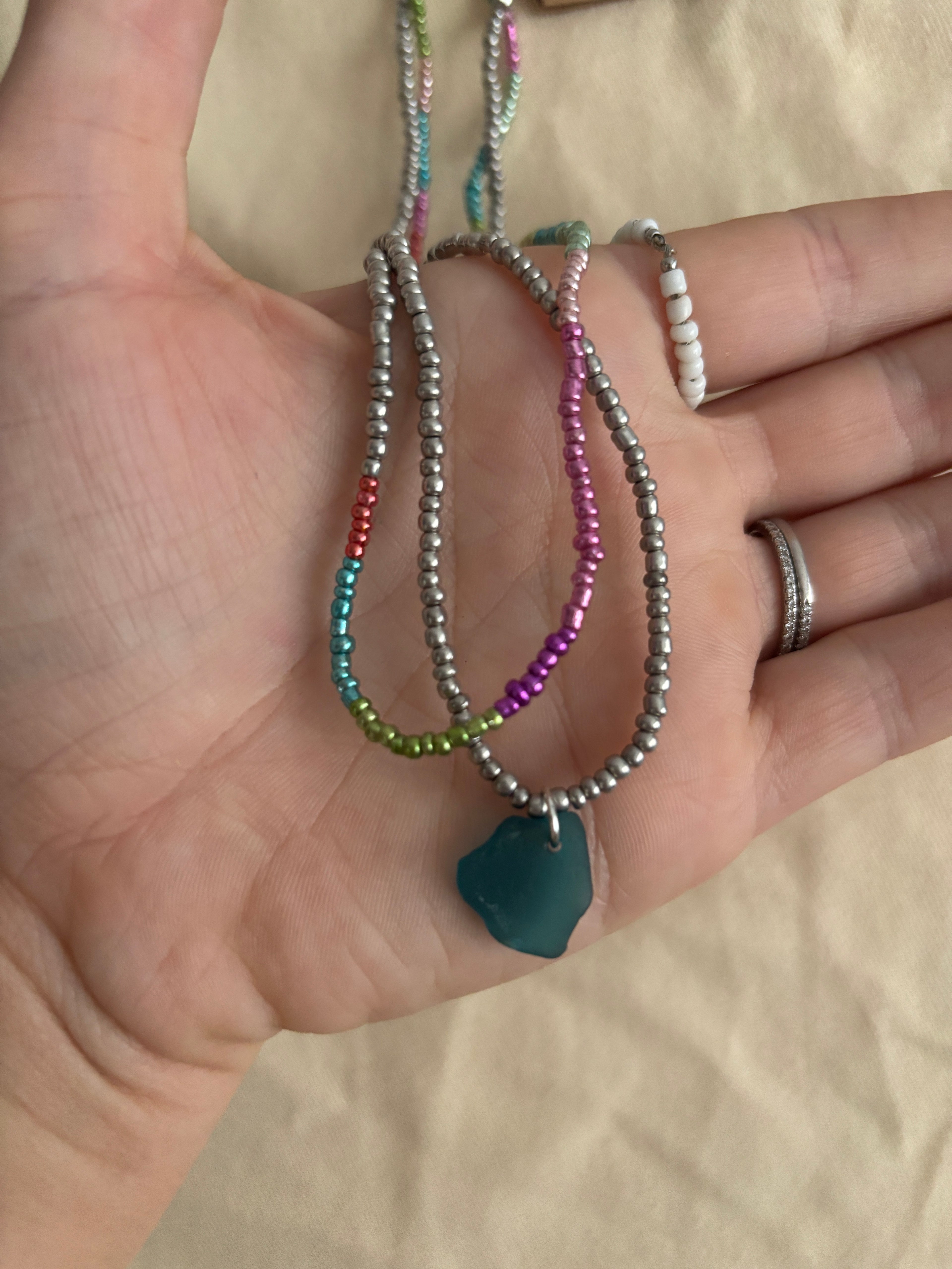 Hand holding multiple beaded bracelets with a plain background