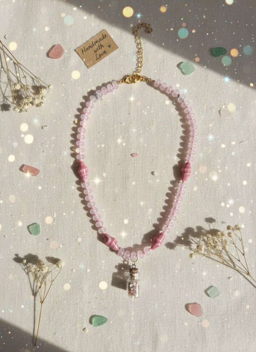 Pink beaded necklace with a pendant on a textured surface with dried flowers and decorative stones.