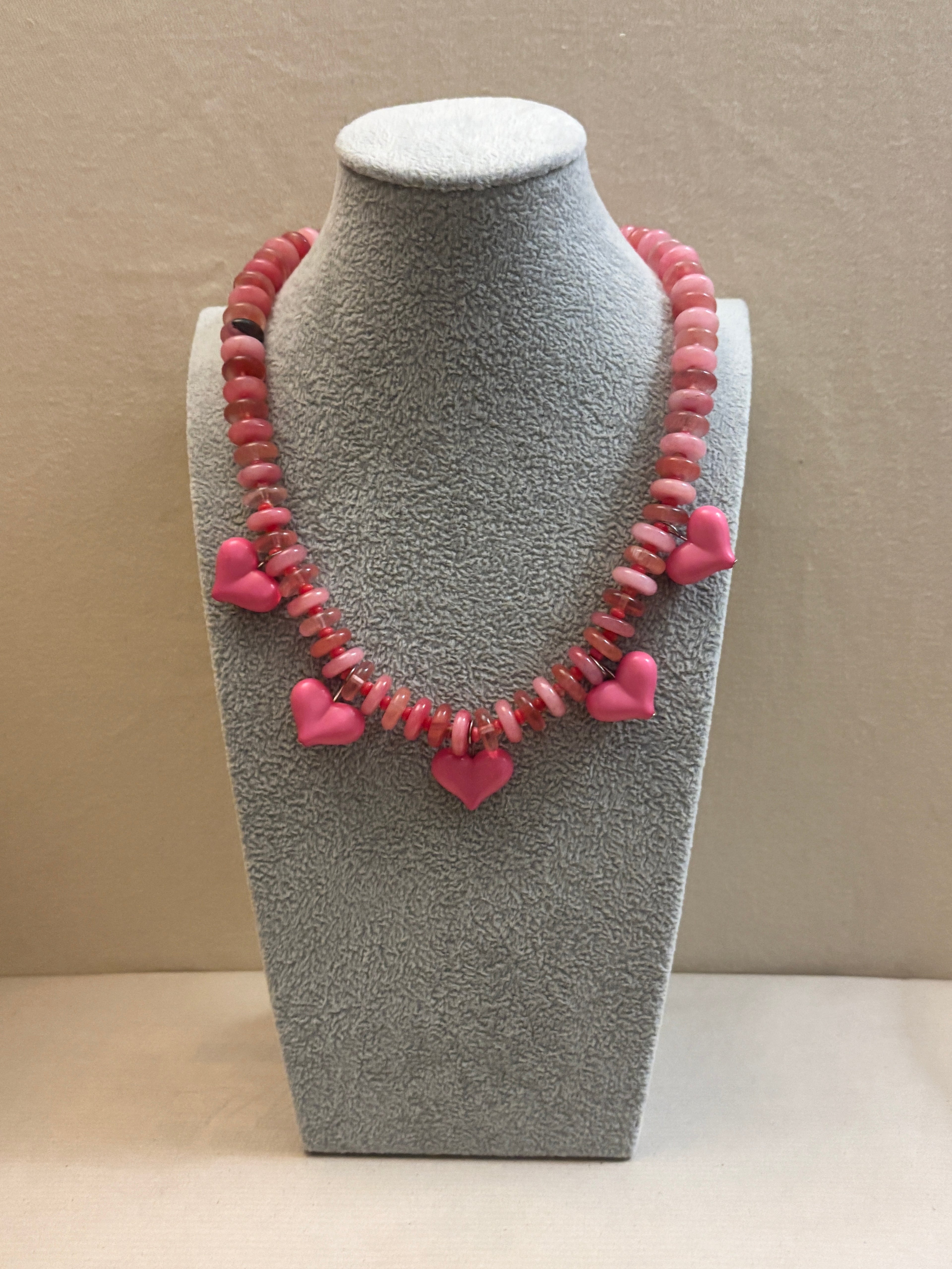 Necklace with pink heart-shaped beads on a gray mannequin bust against a beige background