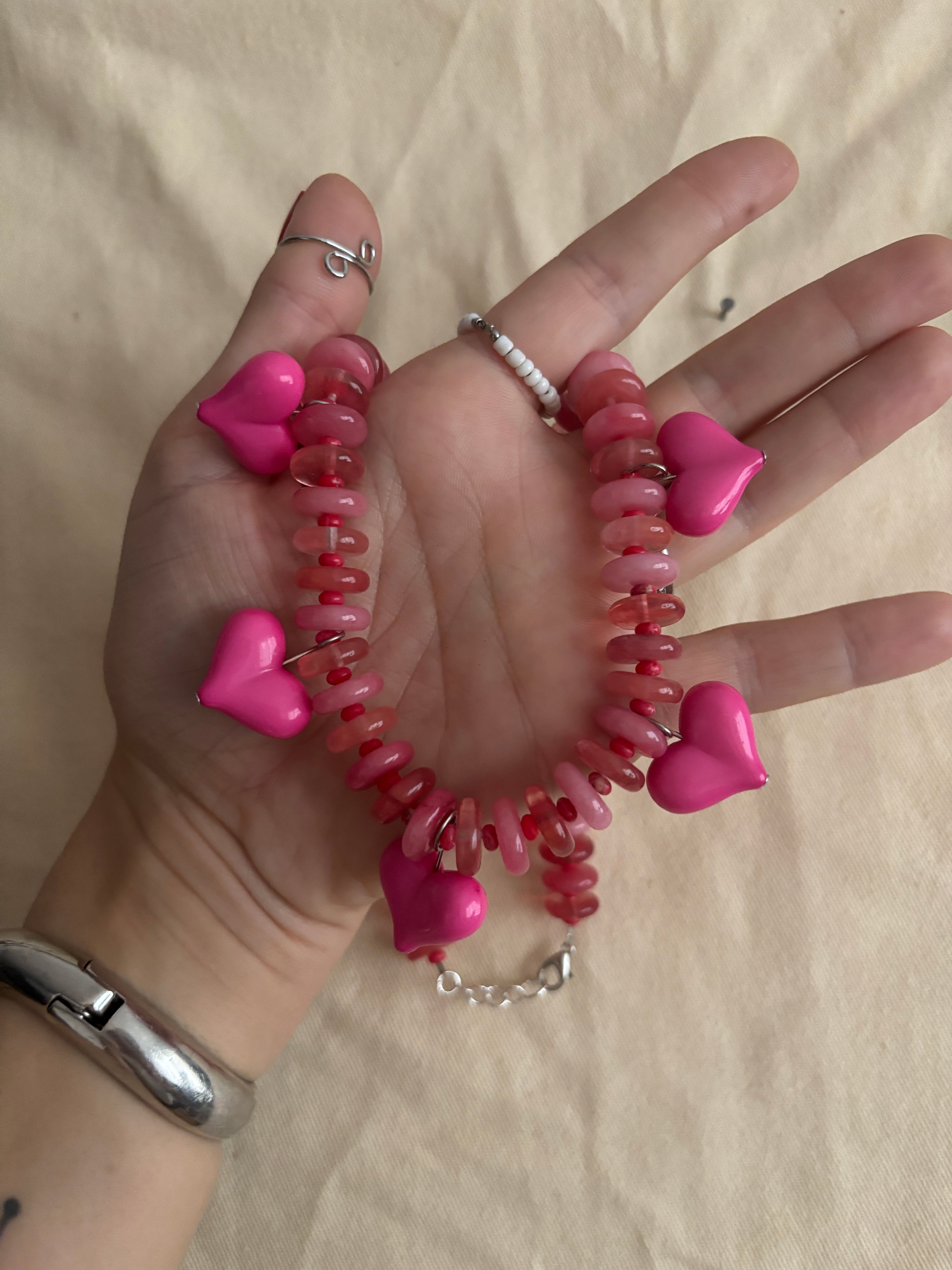Hand holding a pink beaded bracelet with heart-shaped charms on a beige surface