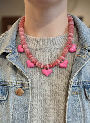 Person wearing a pink heart-shaped beaded necklace with a denim jacket.