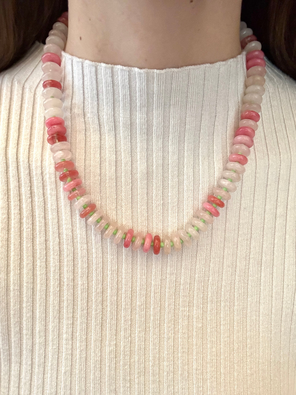 Necklace with pink and white beads on a person wearing a white ribbed top.