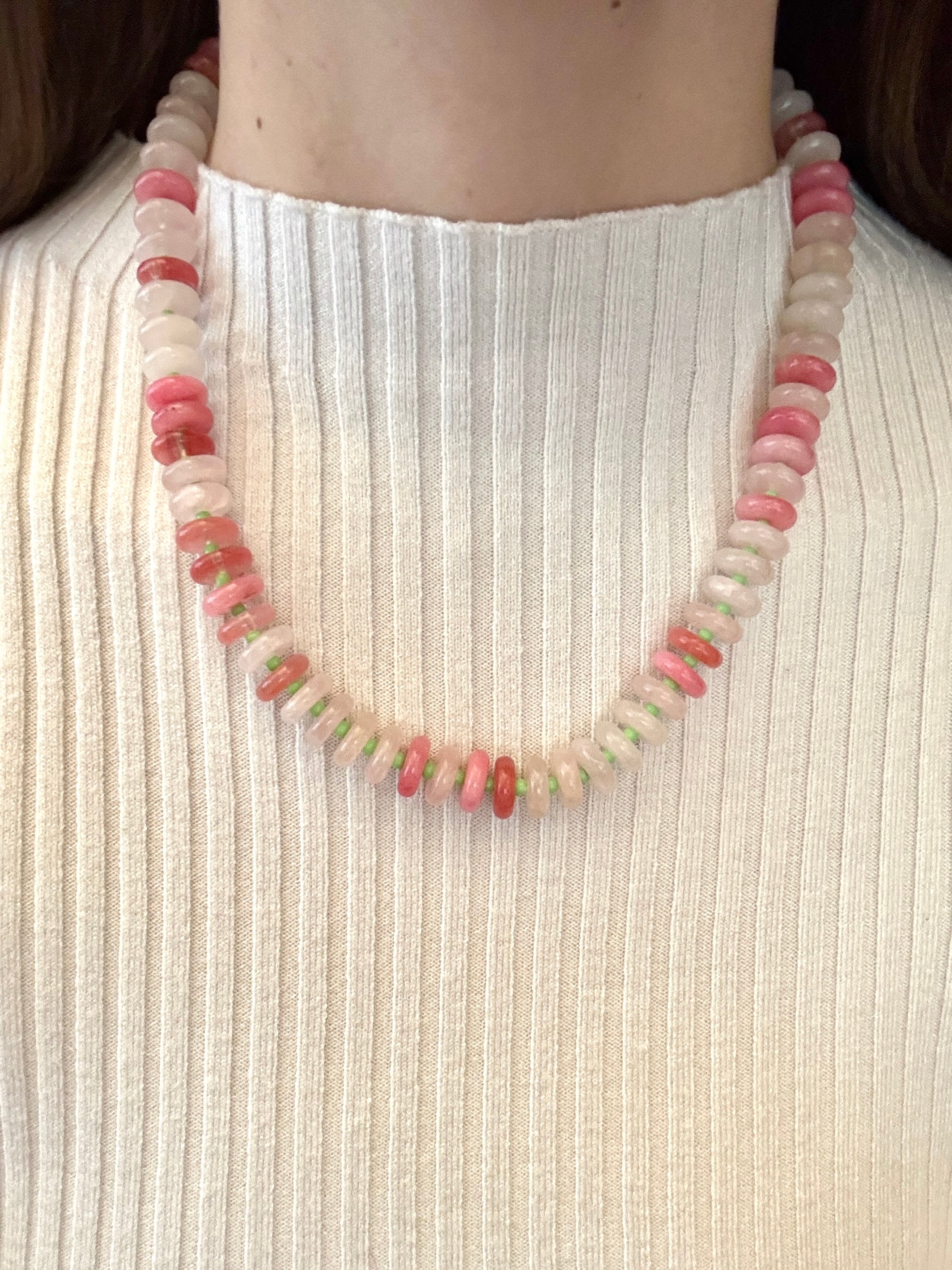 Necklace with pink and white beads on a person wearing a white ribbed top.