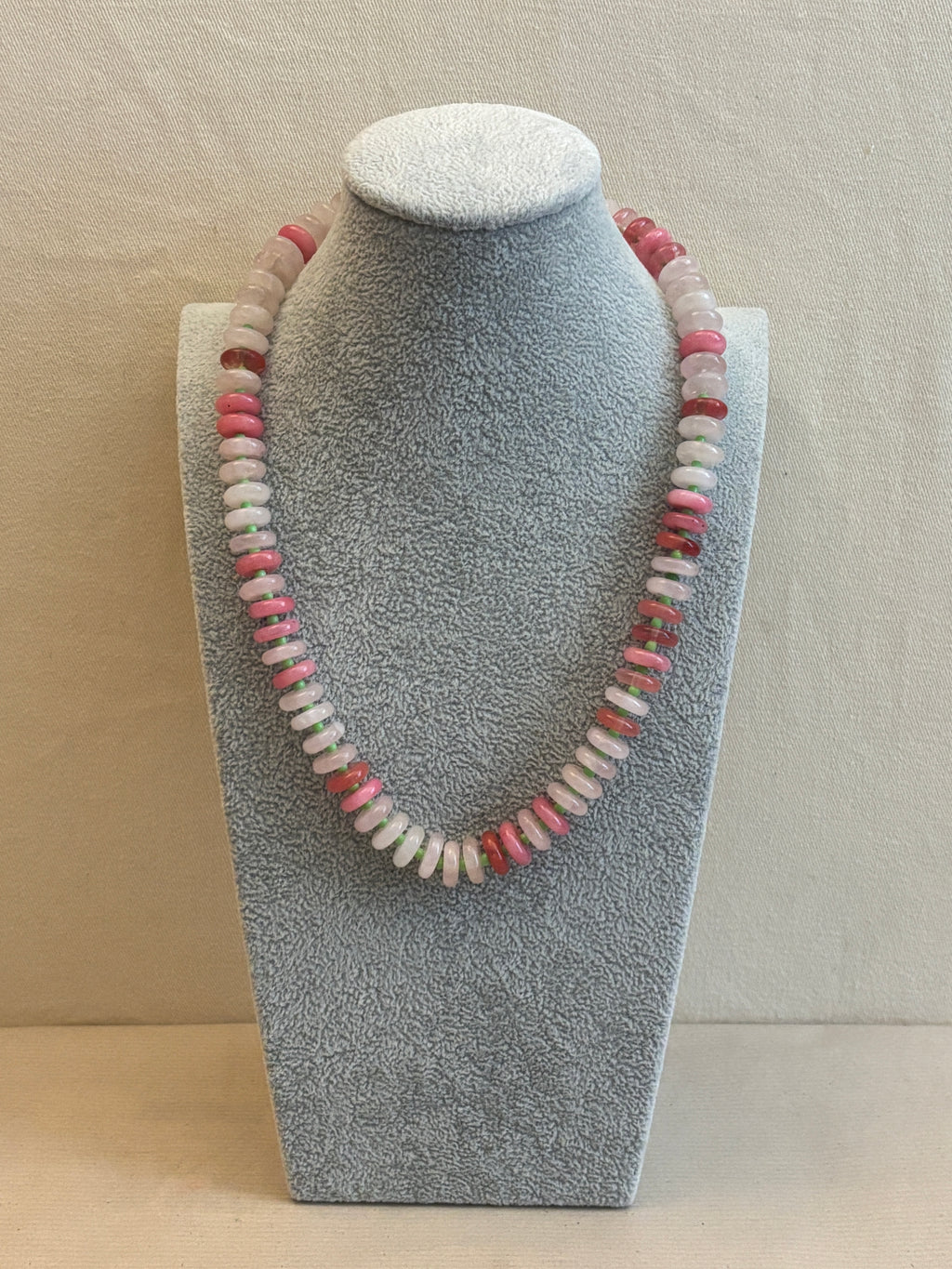 Necklace with pink and white beads on a gray stand against a beige background