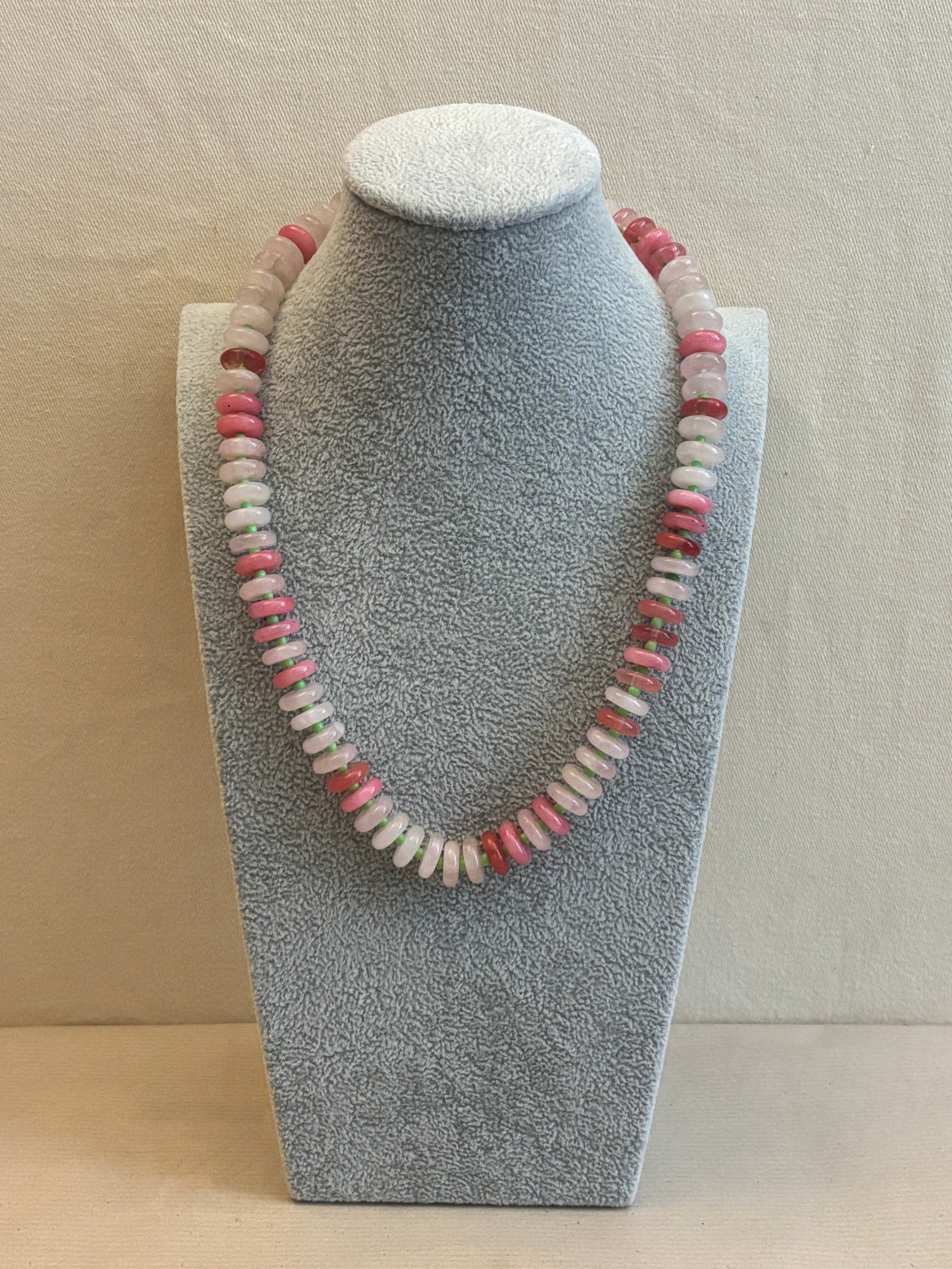 Necklace with pink and white beads on a gray stand against a beige background