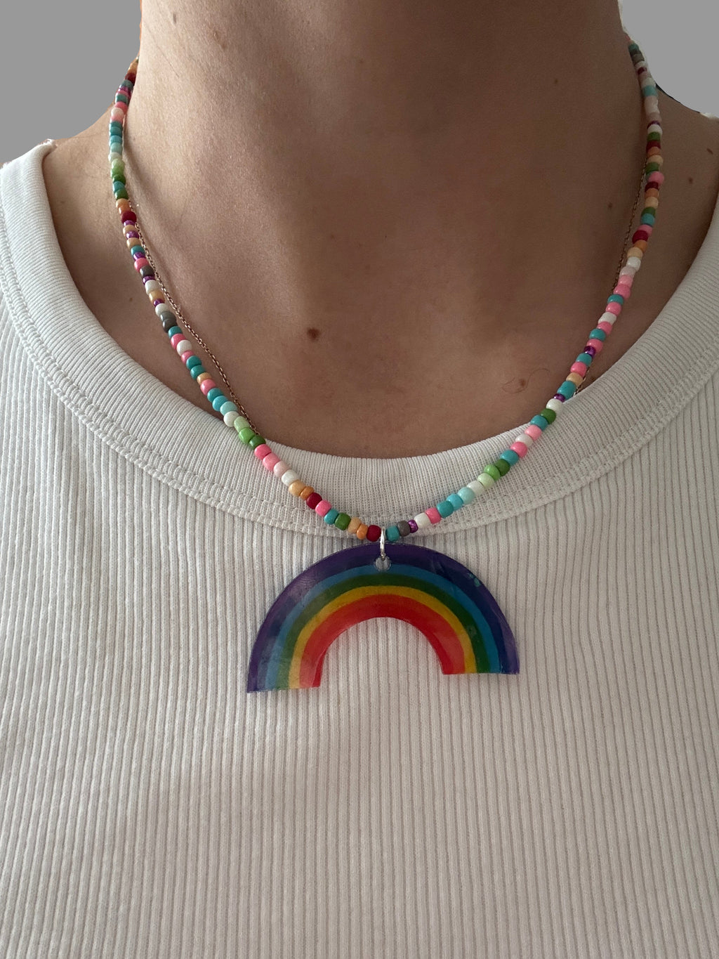 Person wearing a colorful beaded necklace with a rainbow pendant on a striped fabric background