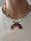 Person wearing a colorful beaded necklace with a rainbow pendant on a striped fabric background