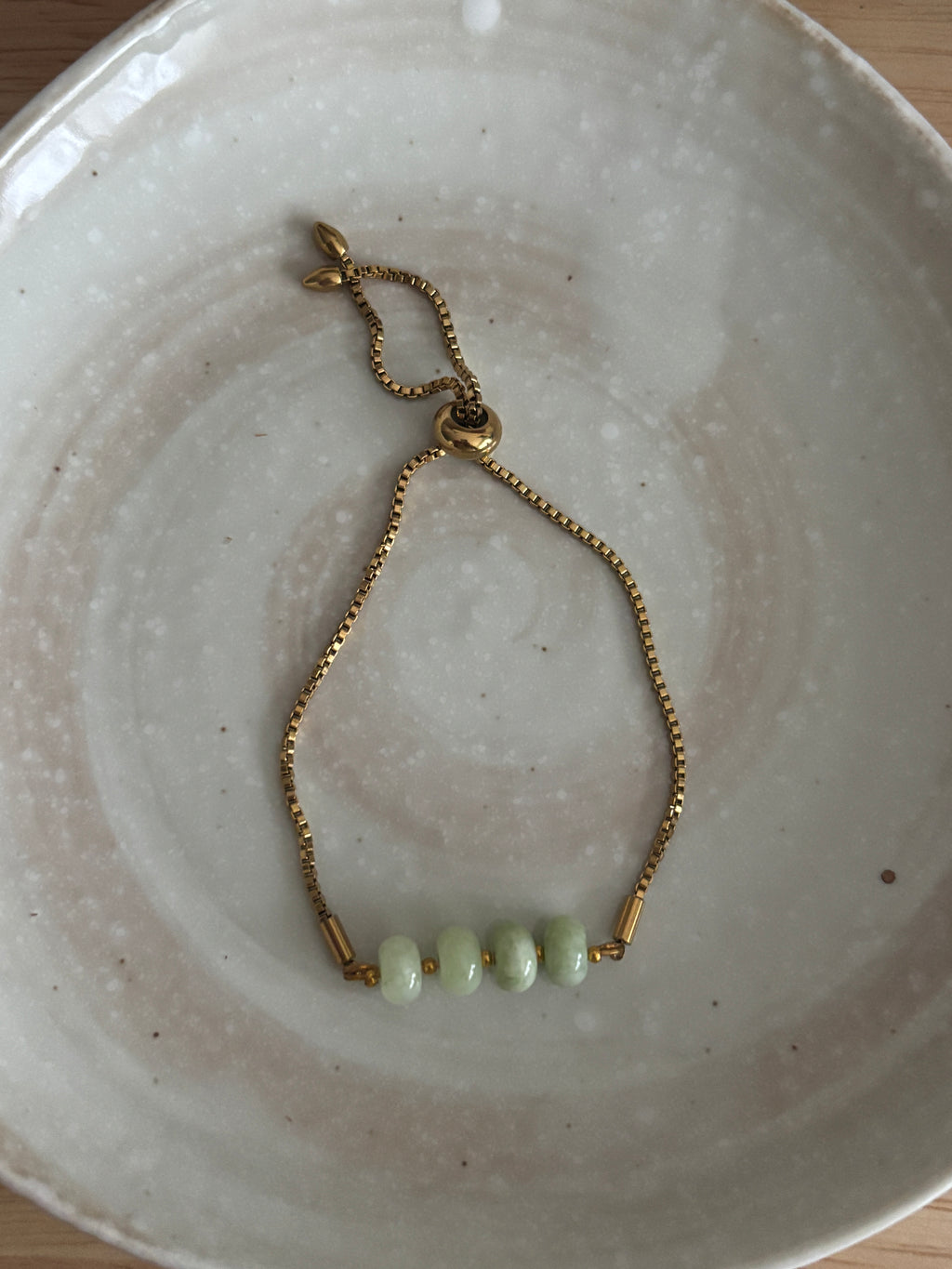 Gold bracelet with green beads on a white ceramic plate